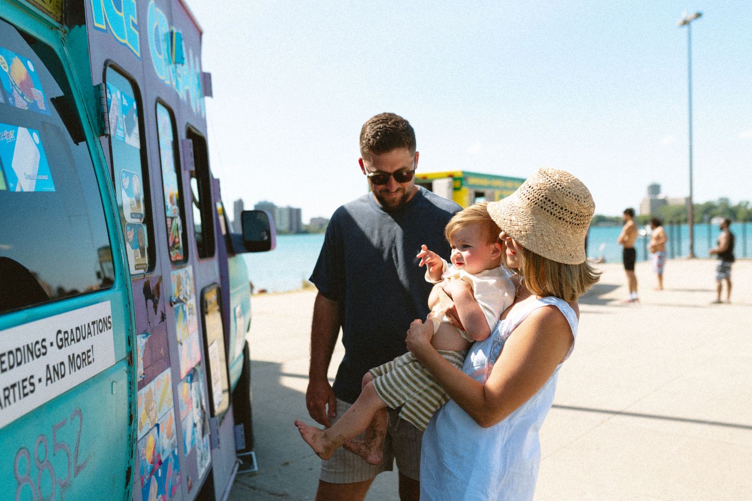 Young family with newborn baby stopping at a colorful ice cream truck on a sunny day.