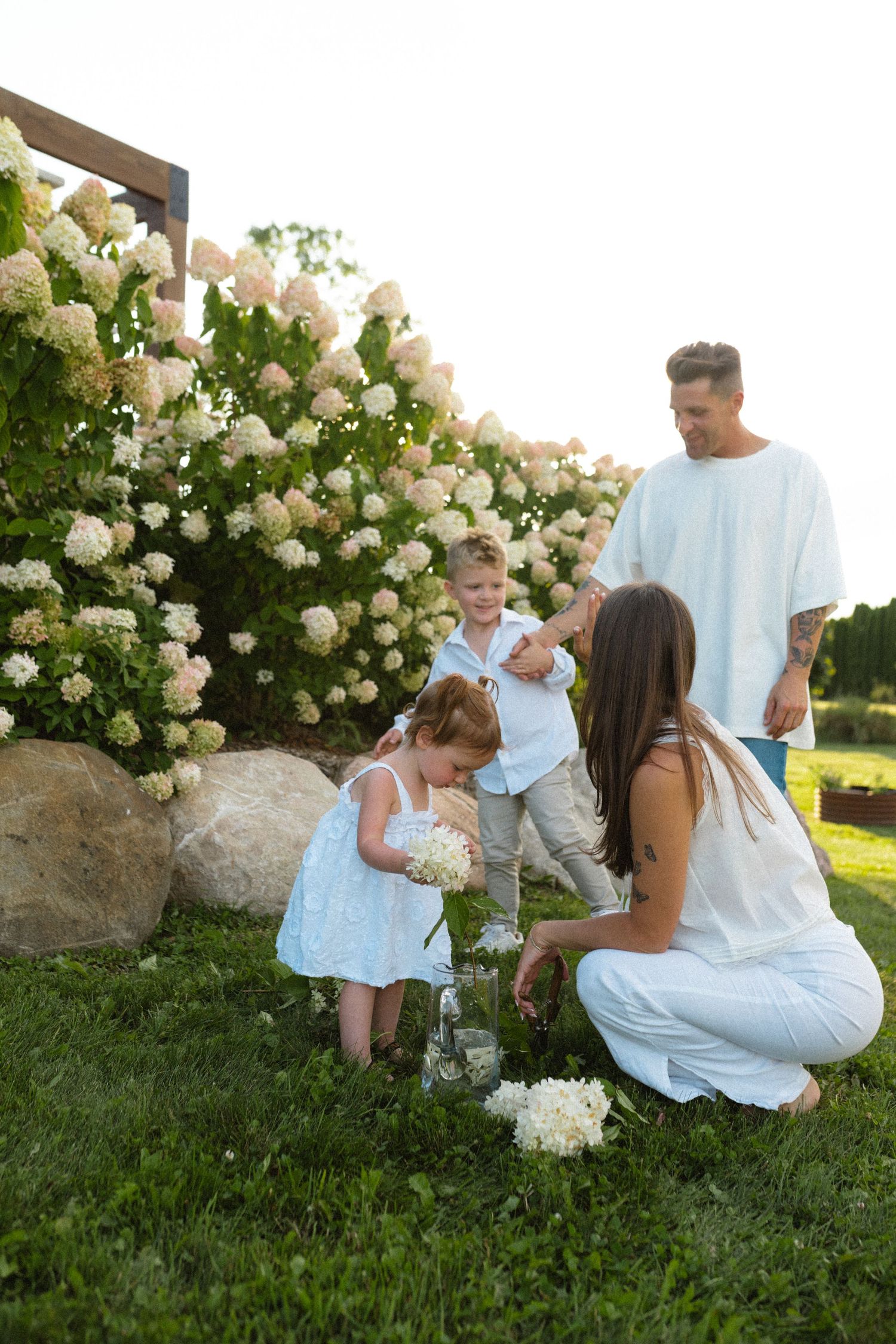 A family of four enjoys a sunny garden moment surrounded by lush white hydrangea bushes.
