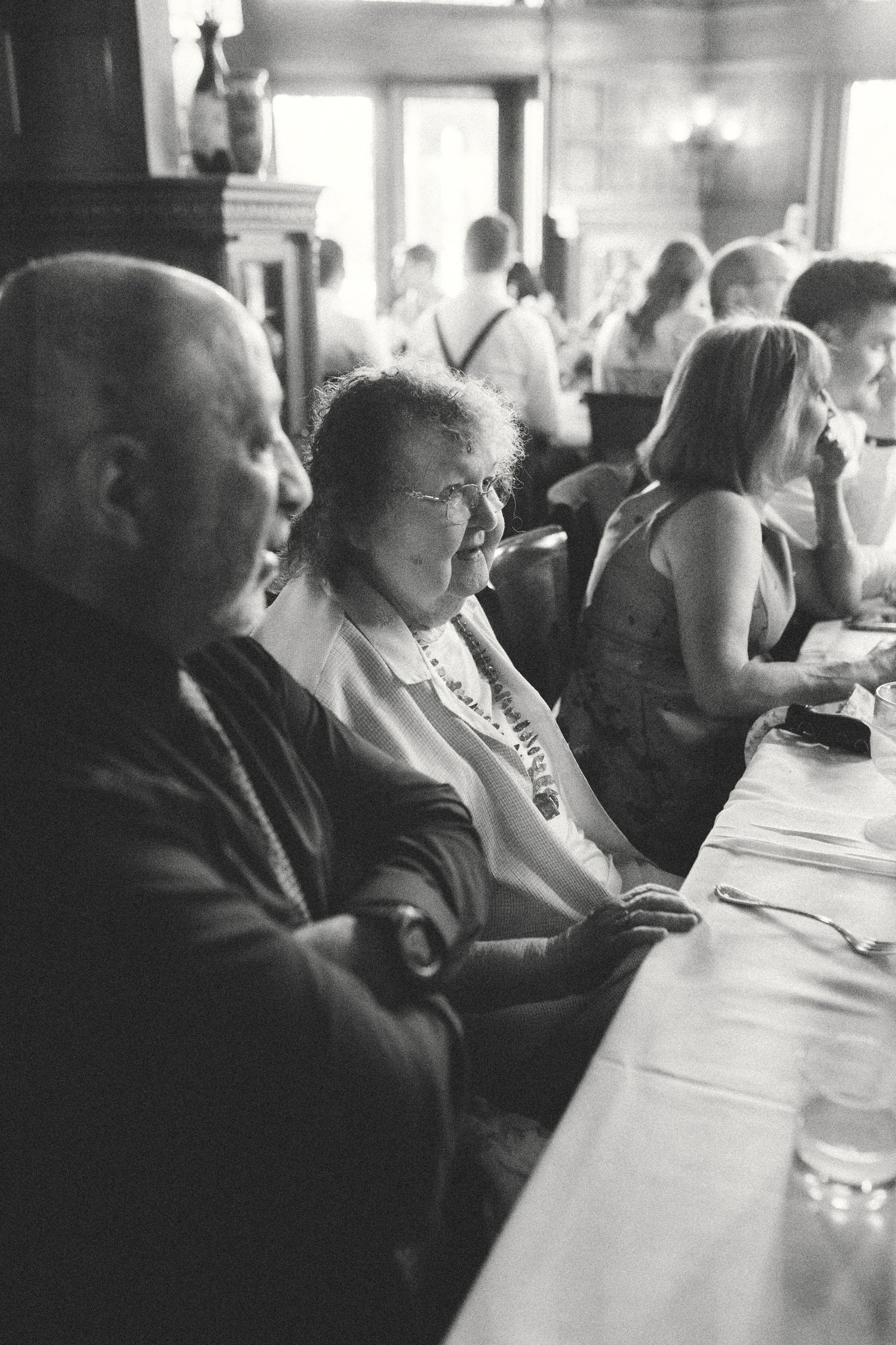 Black and white photo of wedding guests seated at reception dinner table in classic venue.