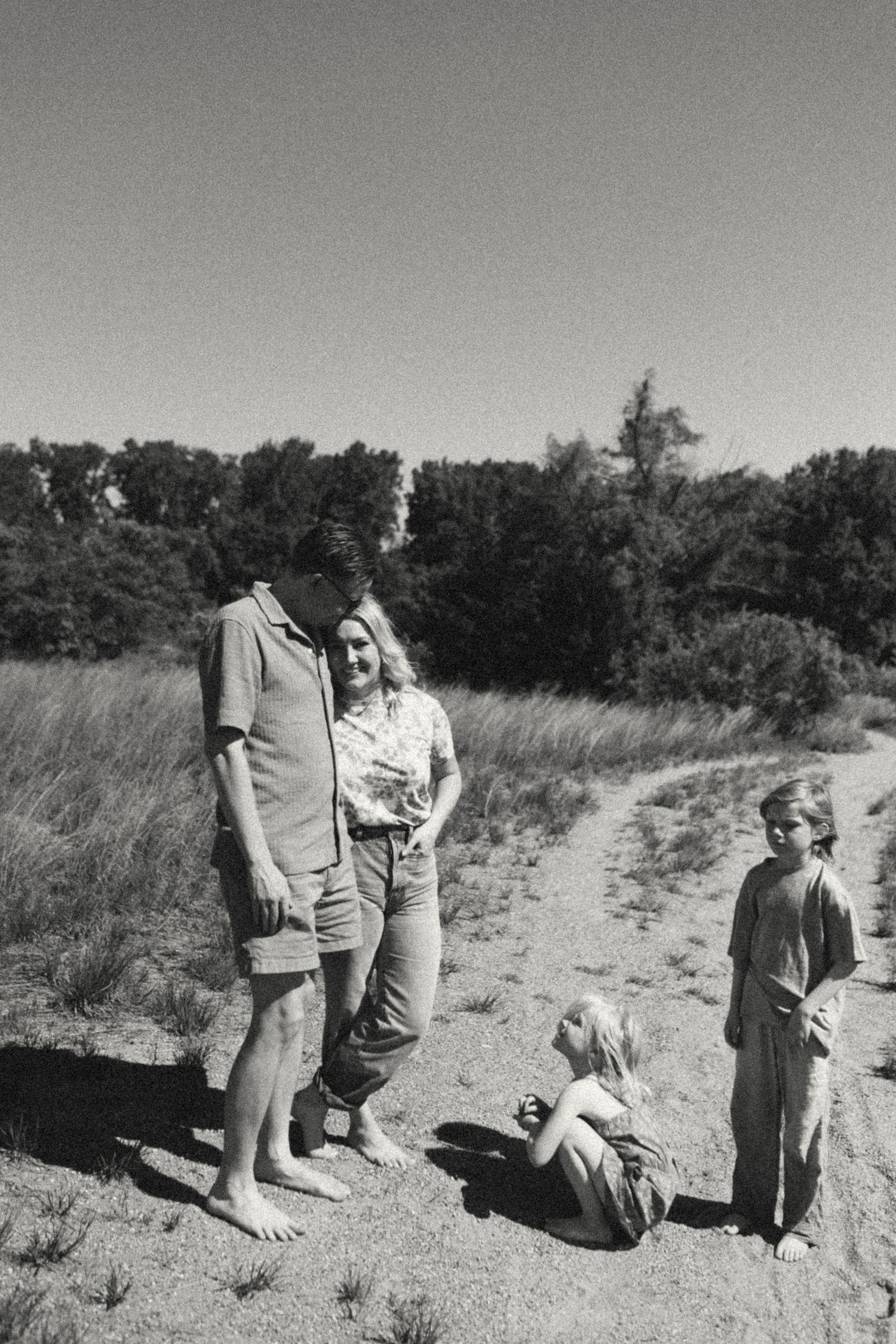 Black and white photo of family with two children standing on sandy rural path outdoors.