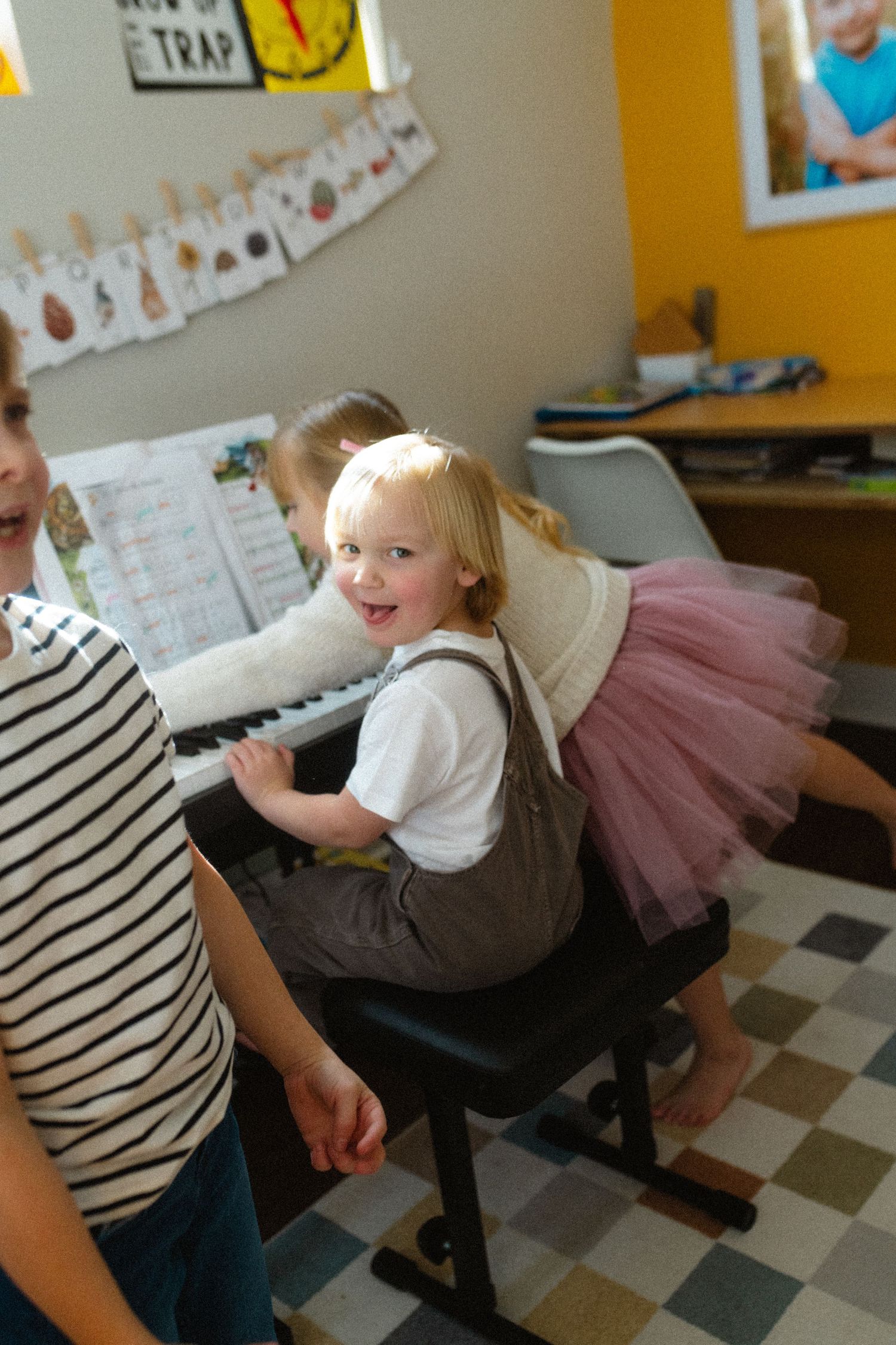 Young blonde girl in a pink tutu smiling while sitting at a white piano.