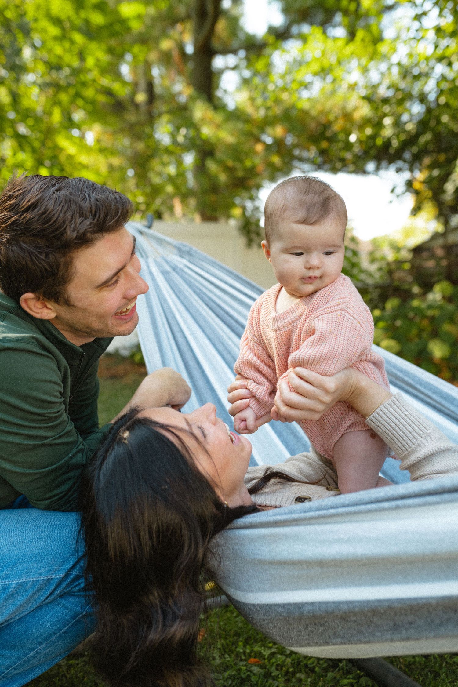 Happy young family with baby relaxing together in a hammock in a sunny green garden.