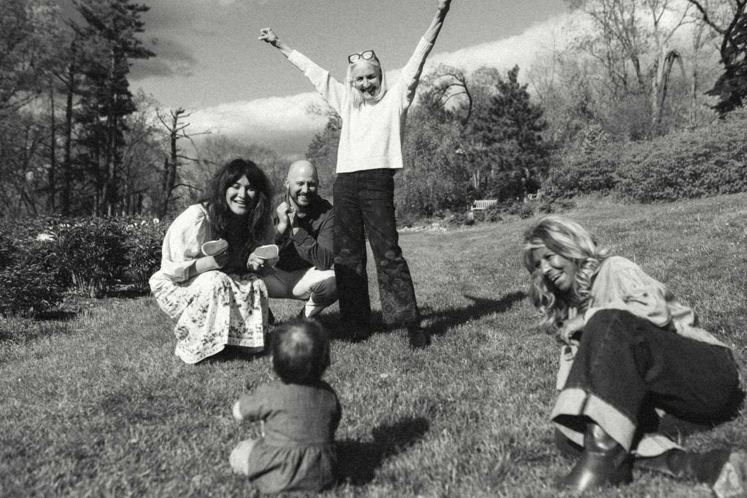 Black and white photo of a joyful family playing together on a grassy lawn outdoors.