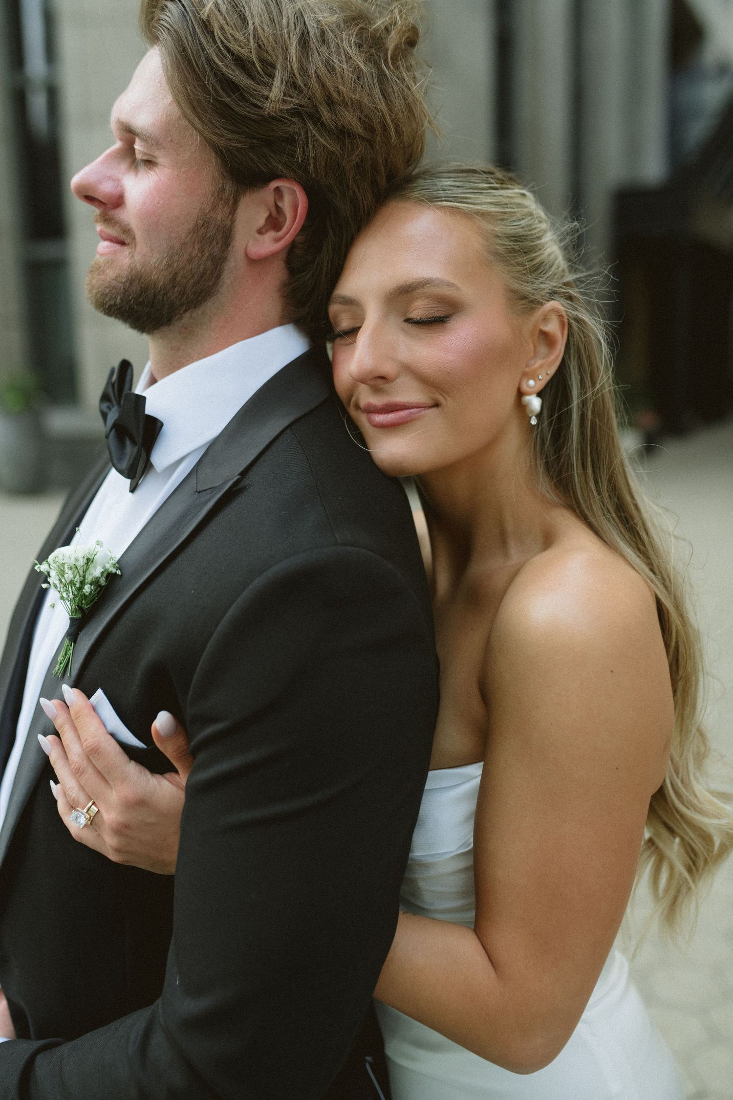 Bride in white strapless gown rests head on groom's back in tender embrace.