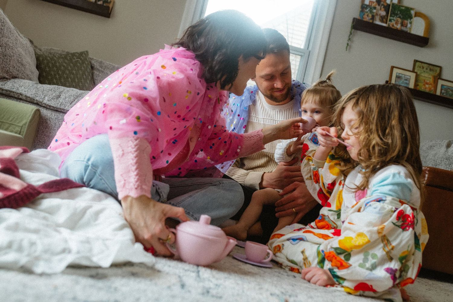 Family with two children enjoying a cozy tea party playtime together on a bed at home.