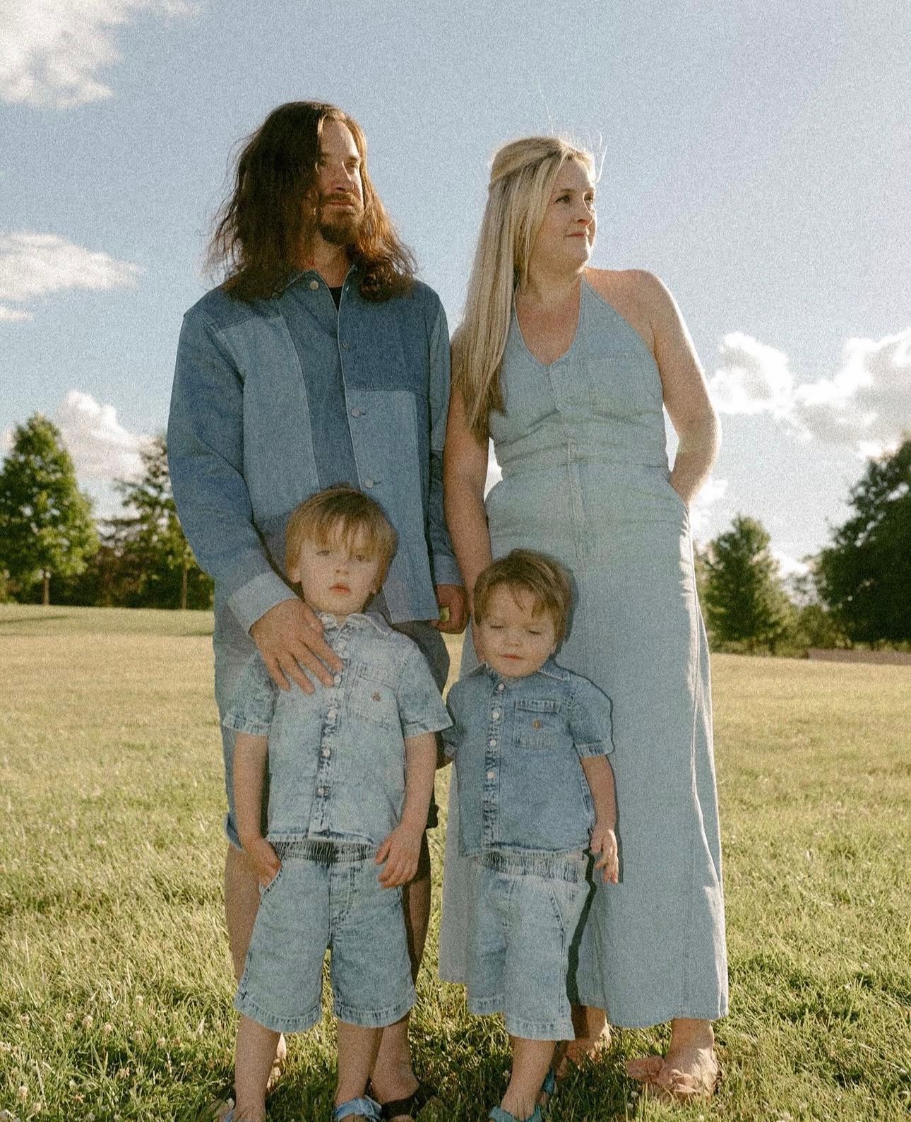 Family of four in matching denim outfits posing on green grass field on a sunny day.