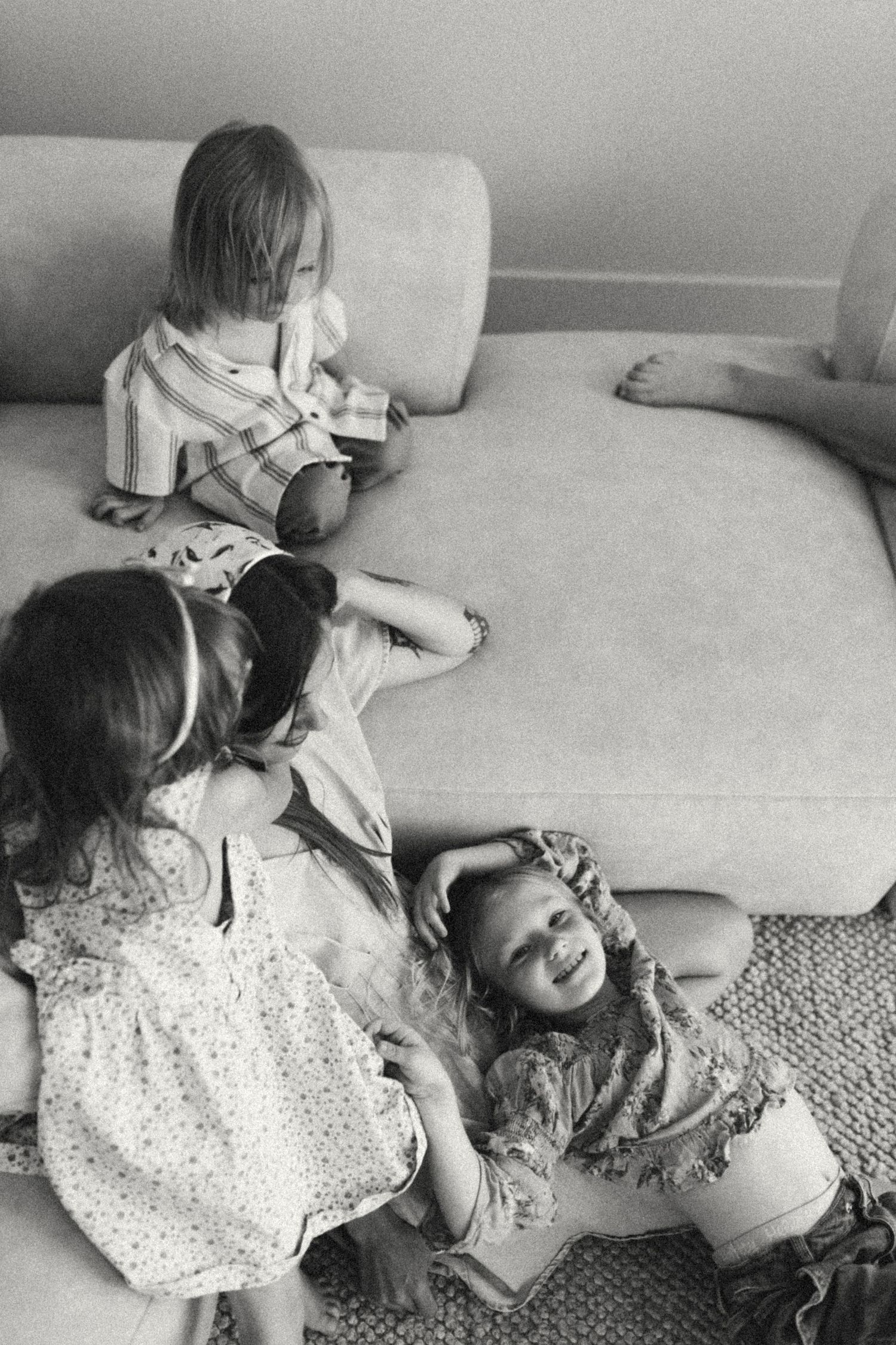 Black and white photo of three young children playing and laughing together near a couch.