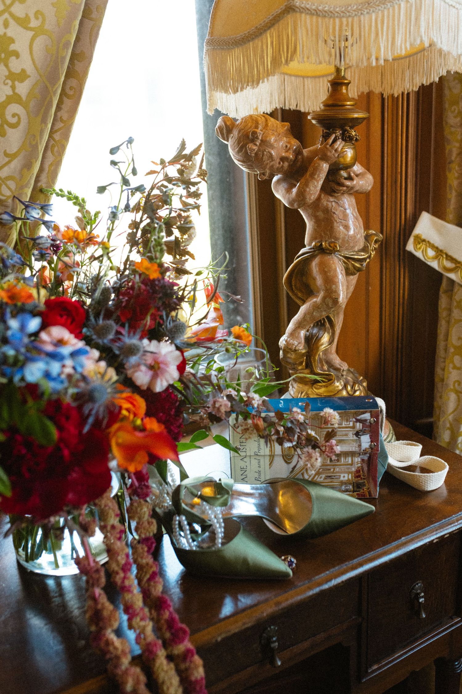 Colorful floral arrangement beside cherub lamp on antique dresser.