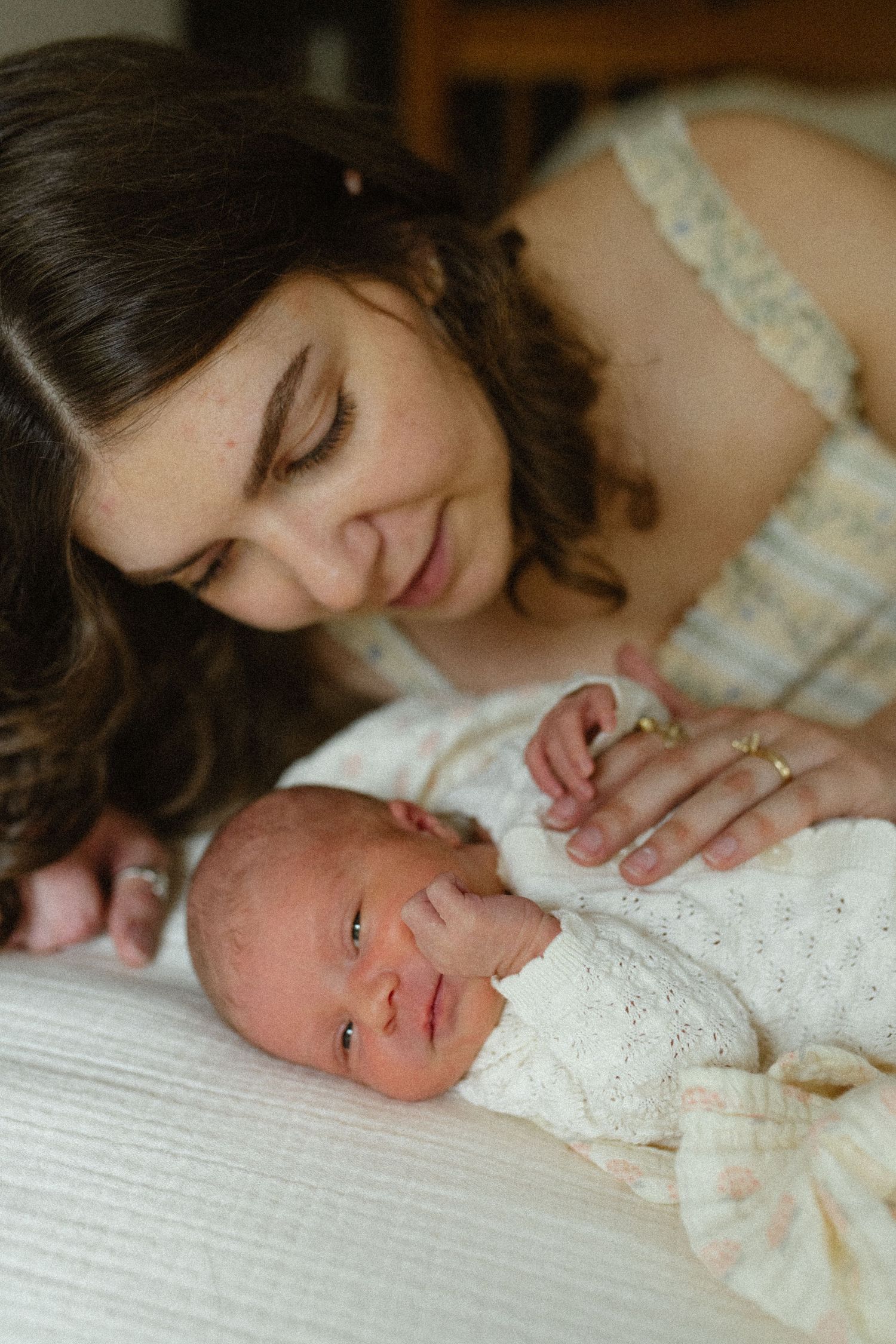 Mother gazing lovingly at alert newborn baby lying on white surface.