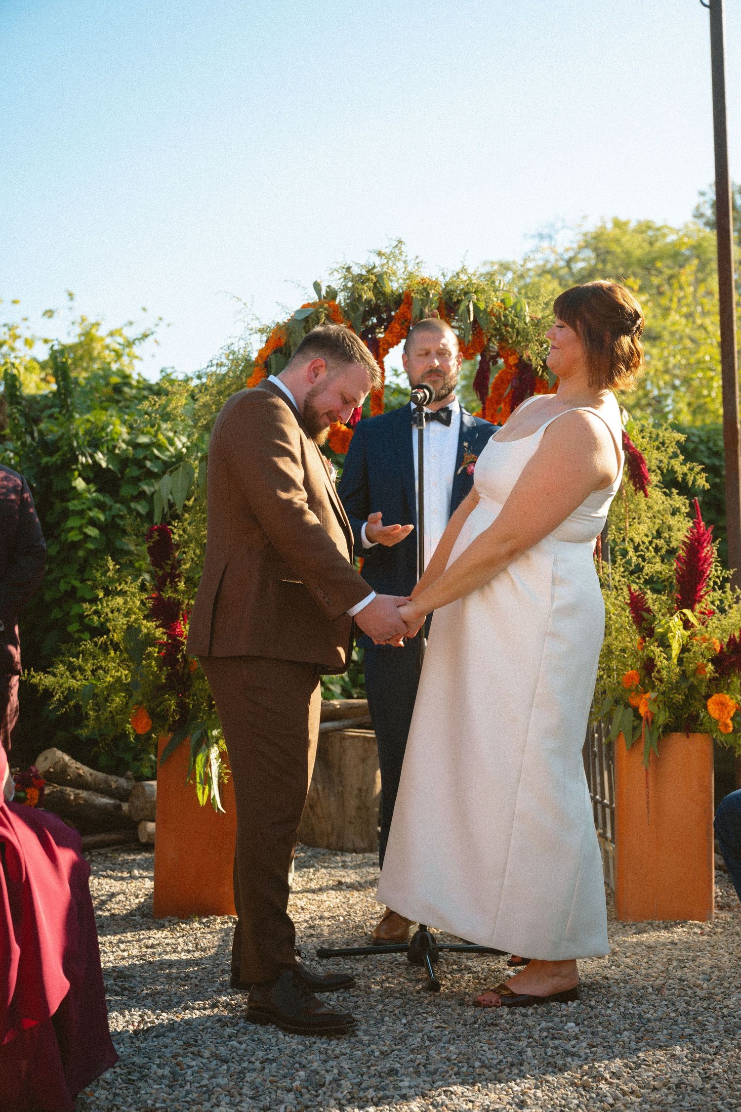 Bride and groom holding hands during outdoor wedding ceremony with colorful floral arch backdrop.