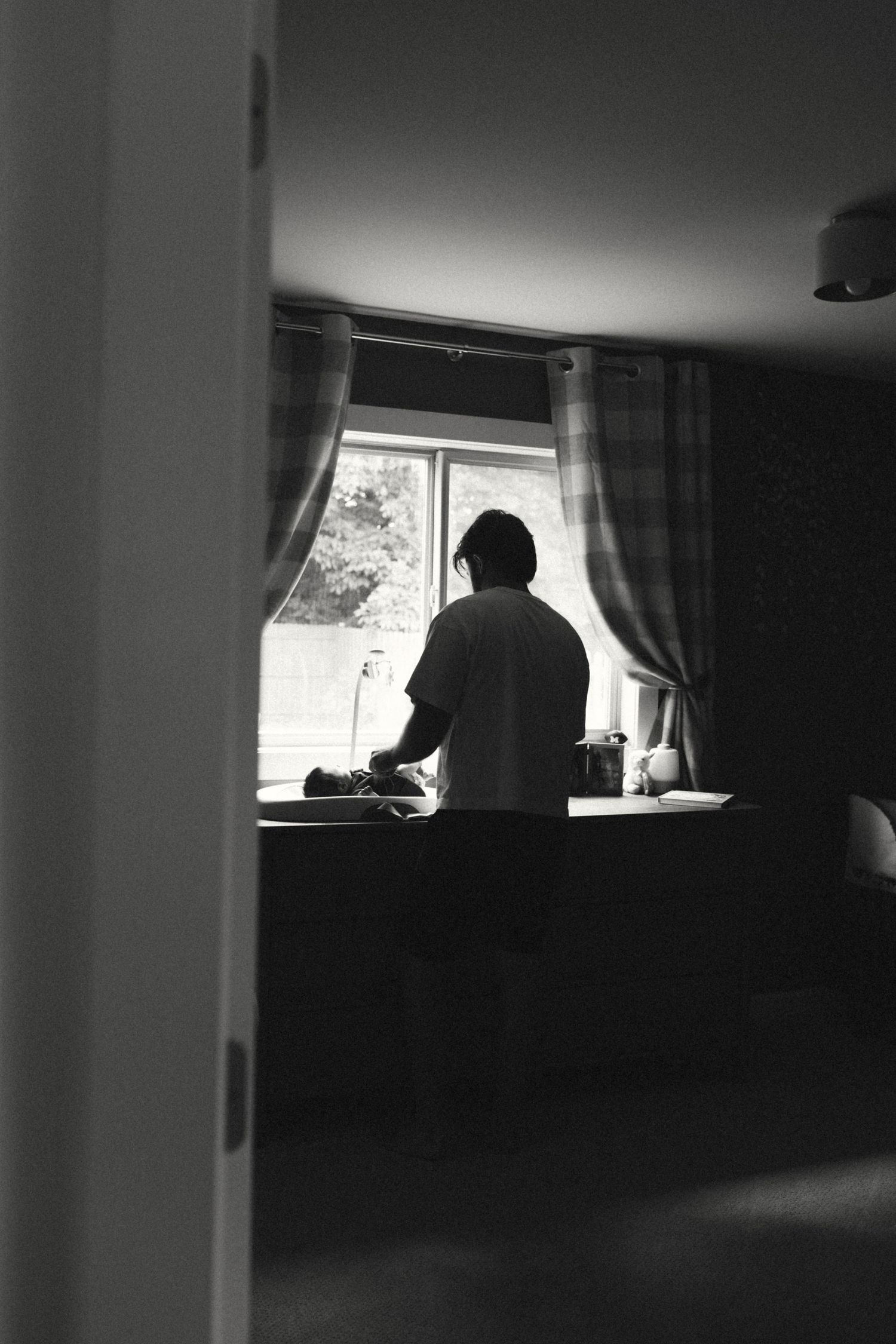 Silhouette of person standing at kitchen window in black and white moody interior photo.