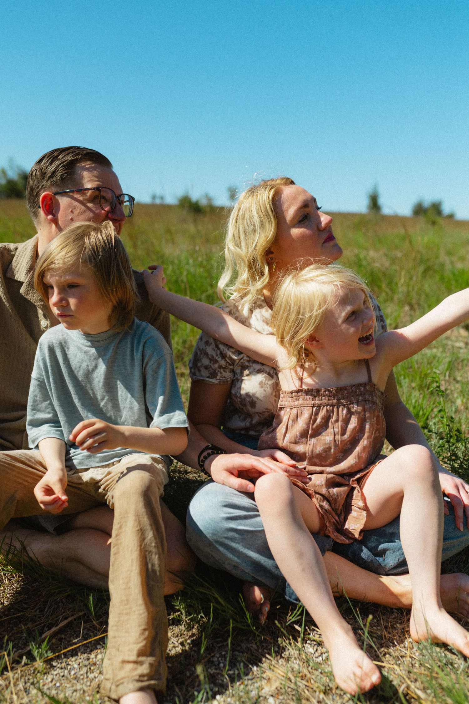 Family of four sitting together on green grass field under clear blue sky on sunny day.