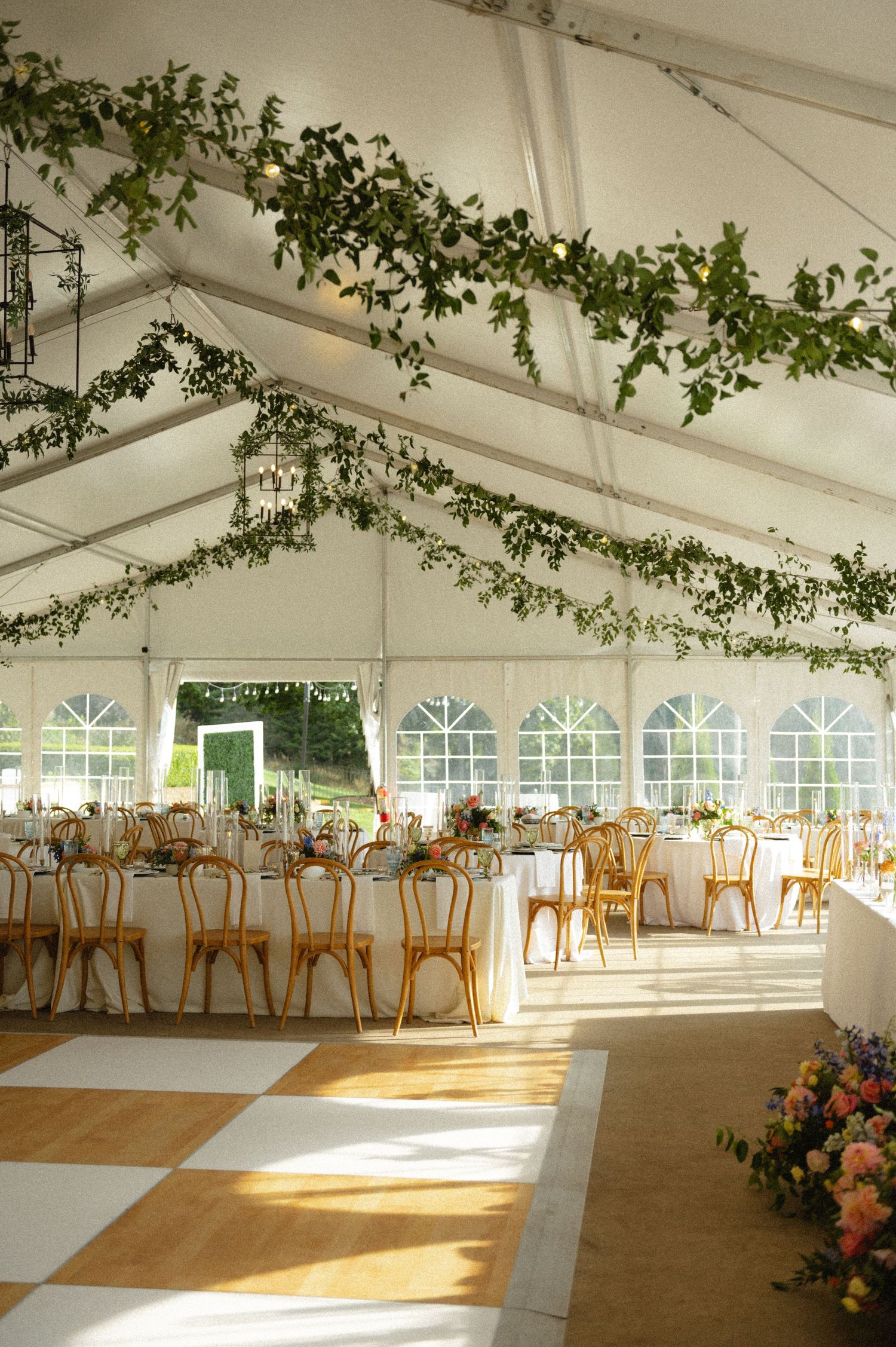 Elegant wedding reception tent with greenery garlands, gold chairs, and checkered dance floor.
