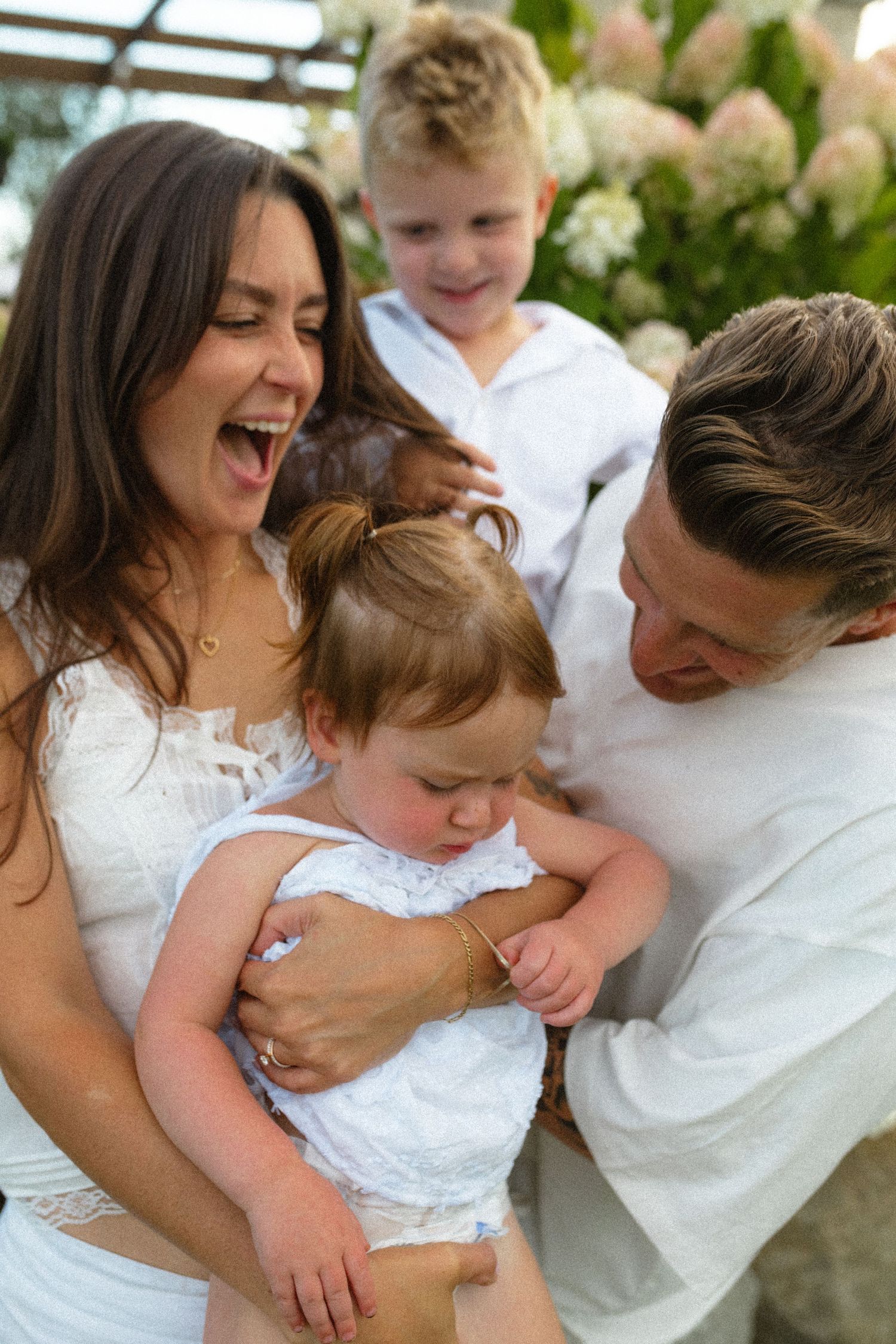 Laughing family of four sharing a joyful moment together outdoors near hydrangea bushes.