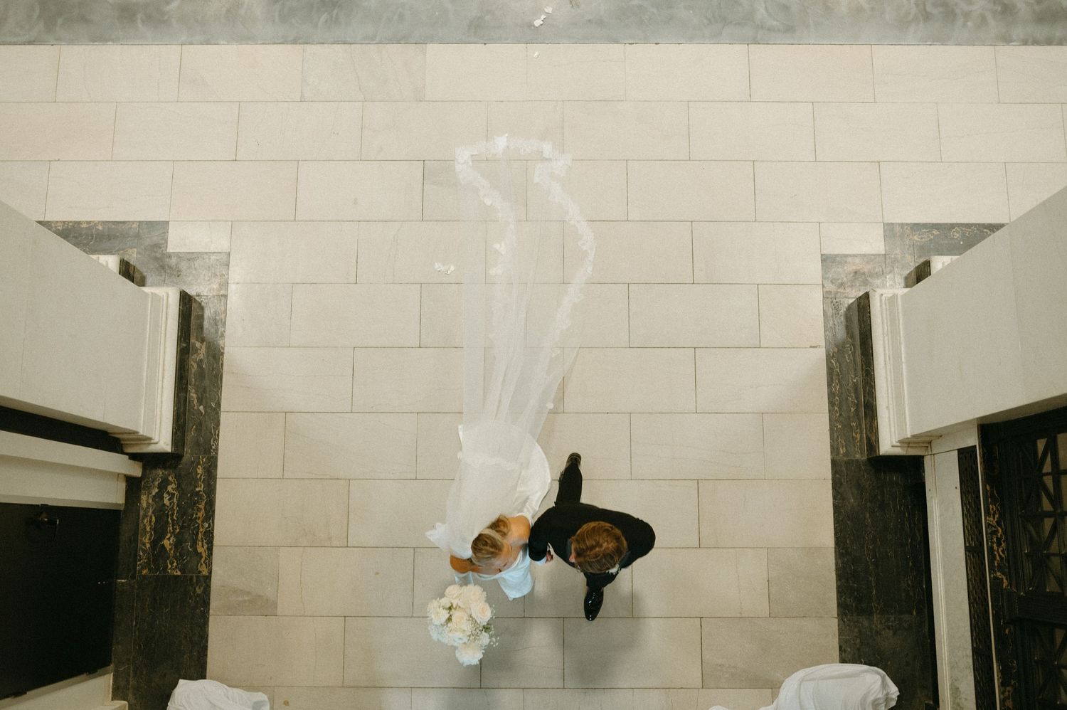 Aerial view of bride and groom standing in marble-floored building atrium.