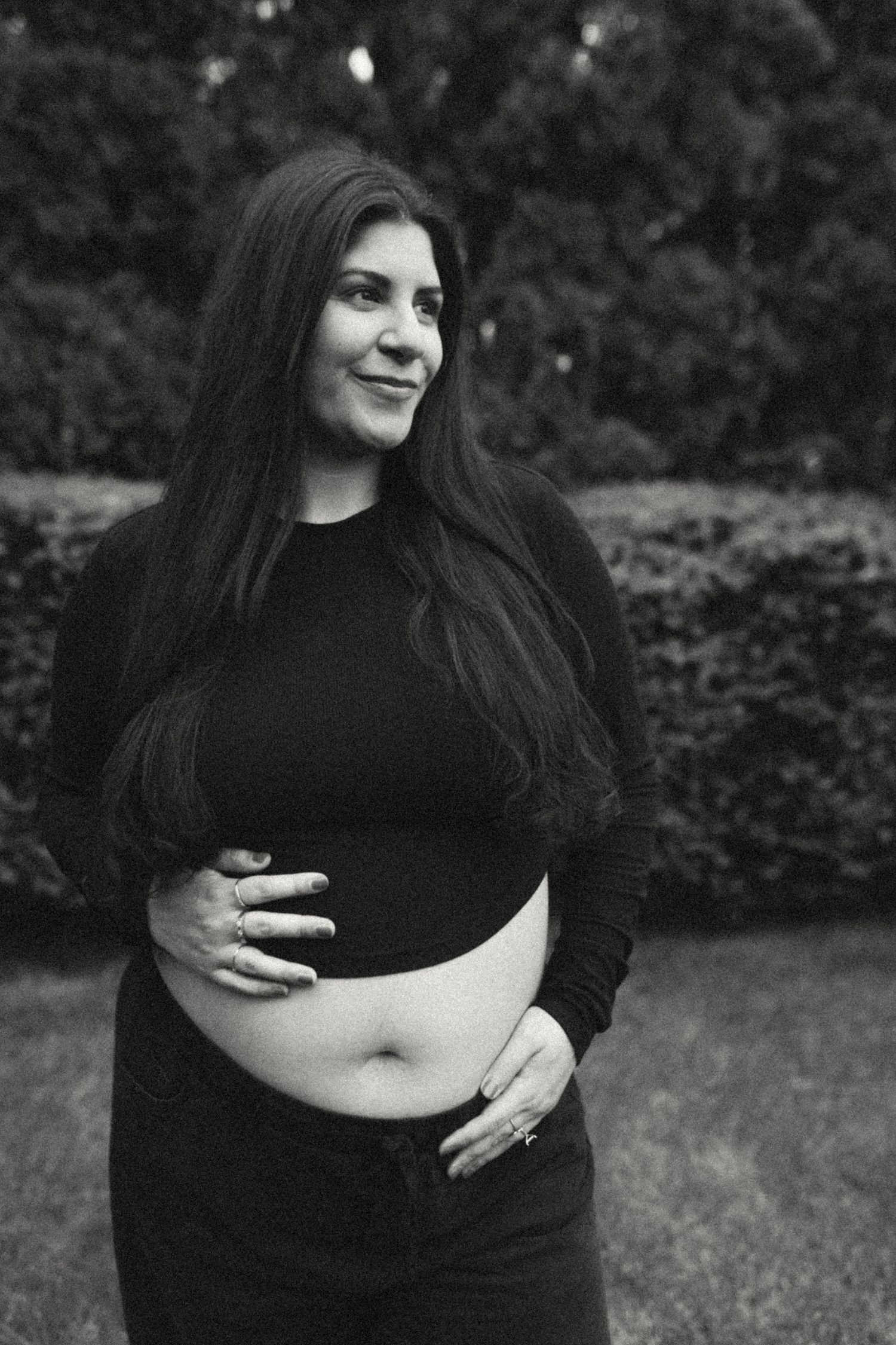 Black and white photo of pregnant woman in black crop top holding baby bump outdoors.