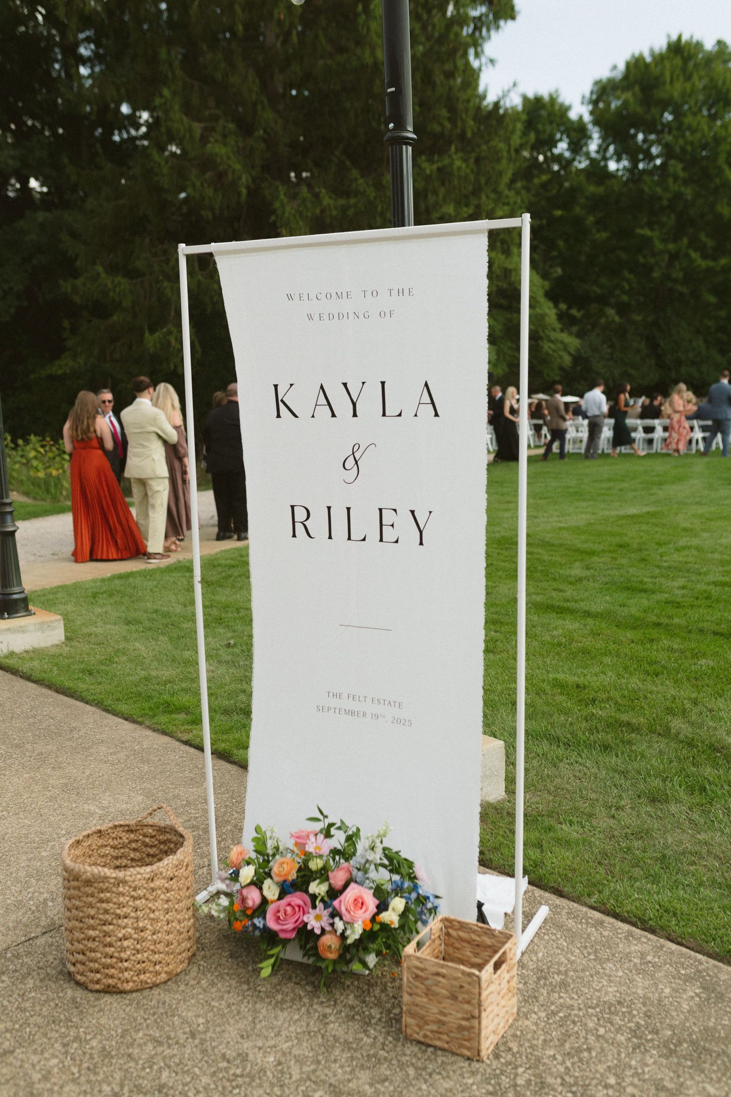 Welcome sign for Kayla and Riley wedding ceremony displayed on white arch with flowers.
