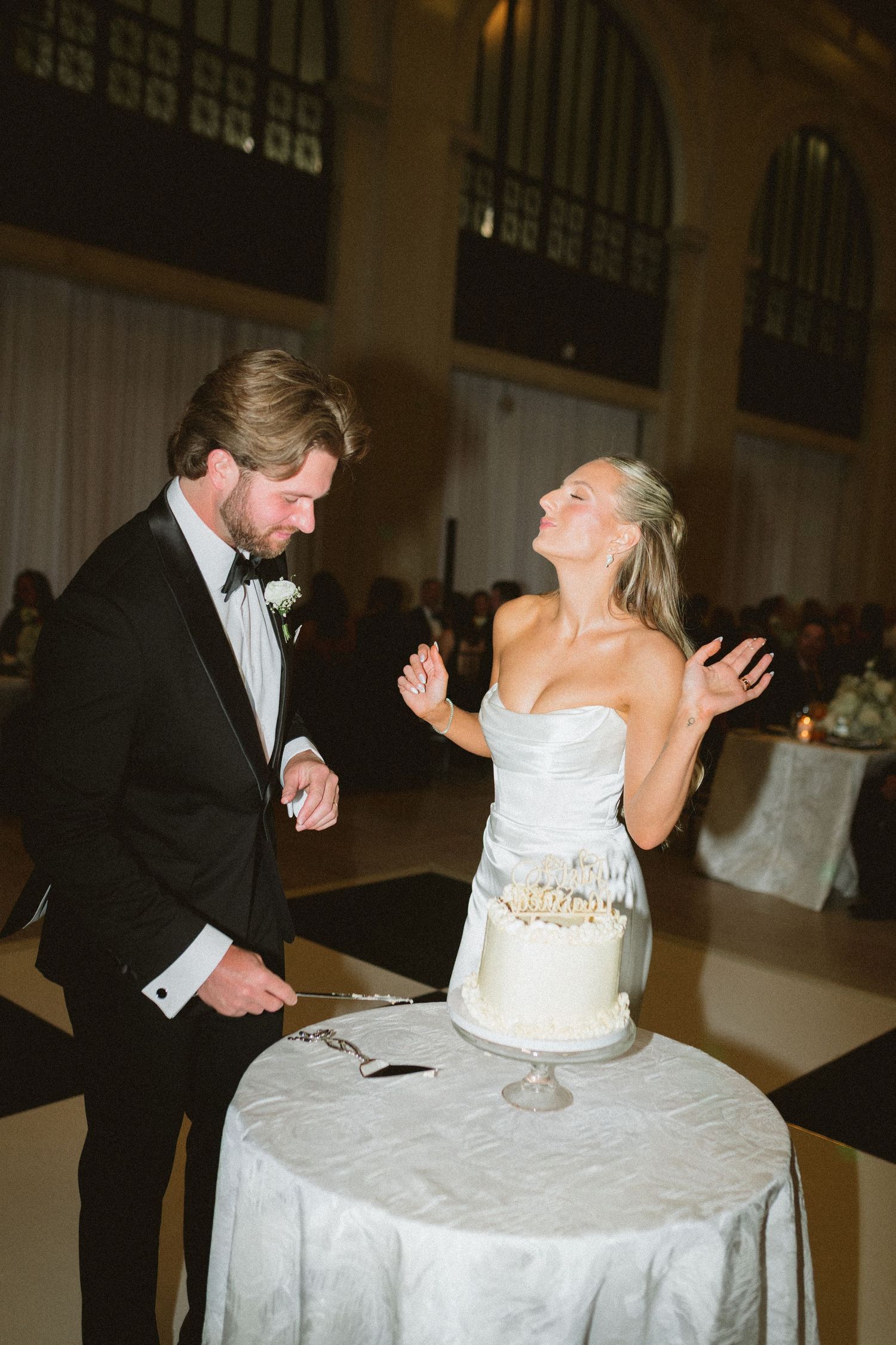 Bride and groom cut white wedding cake at elegant indoor reception venue.