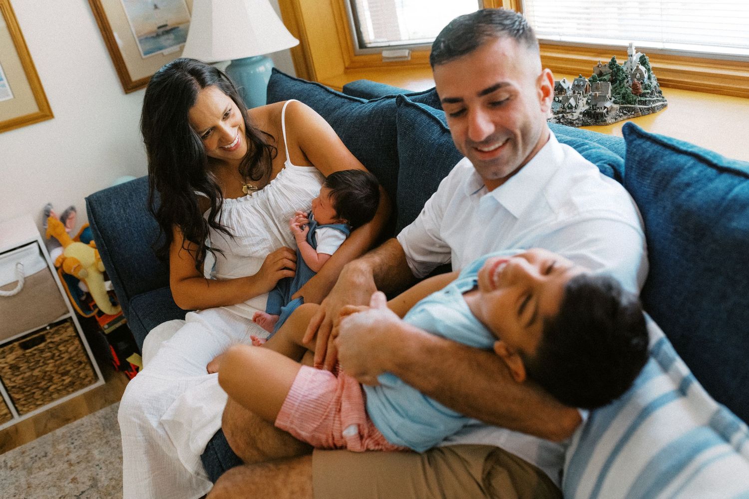 Happy family with two children laughing and bonding together on blue sofa indoors.