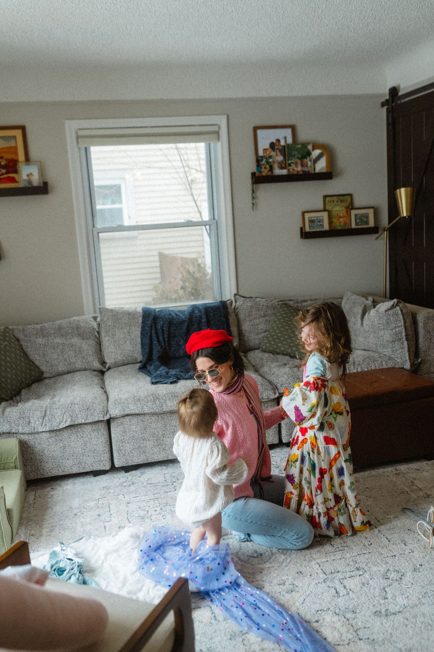 A mother in a red beret plays with her two young daughters in a cozy living room.