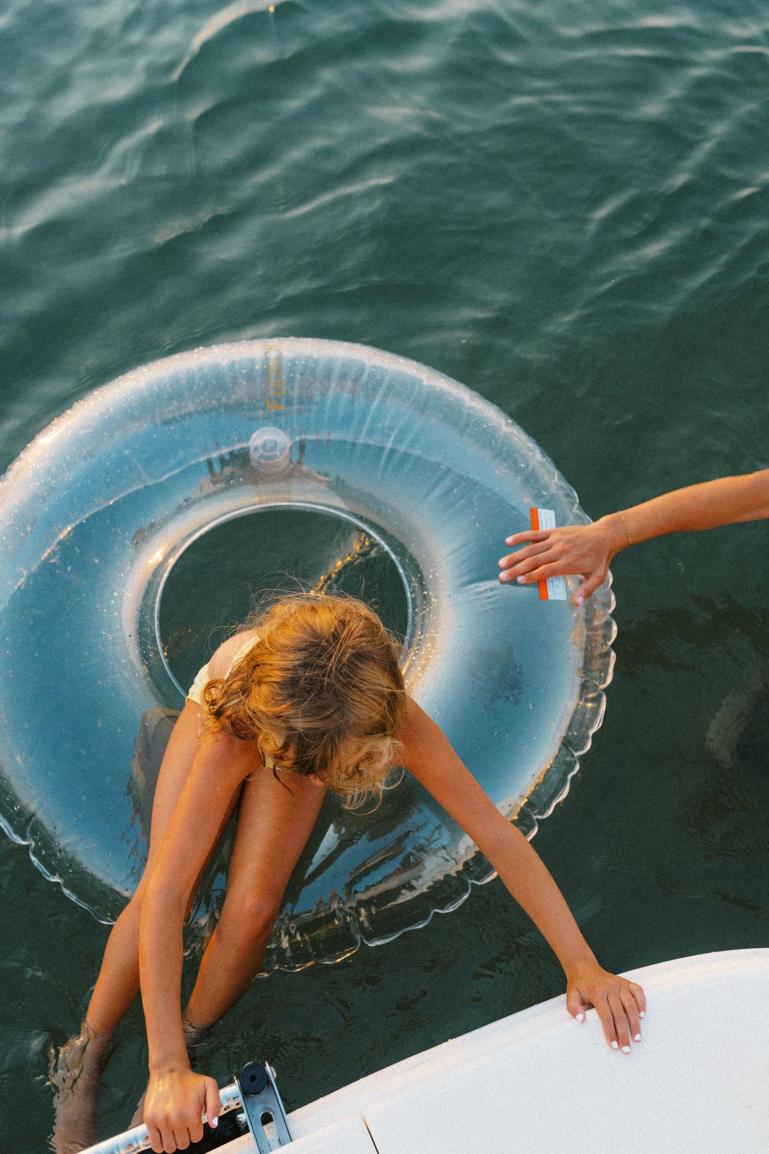 Young girl climbing onto a boat from the water next to a clear inflatable pool ring.