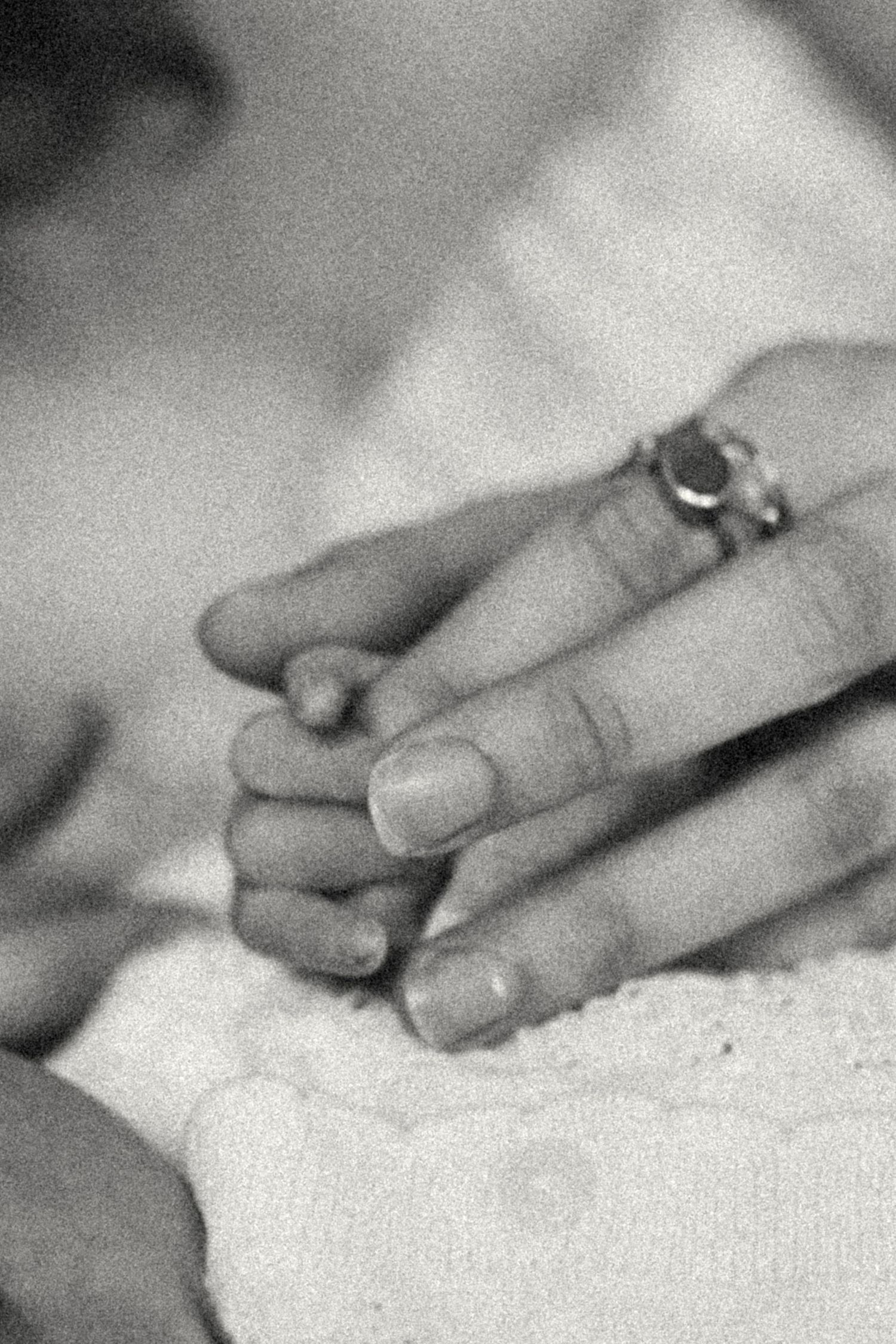 Black and white close-up of newborn baby grasping mothers finger with ring.