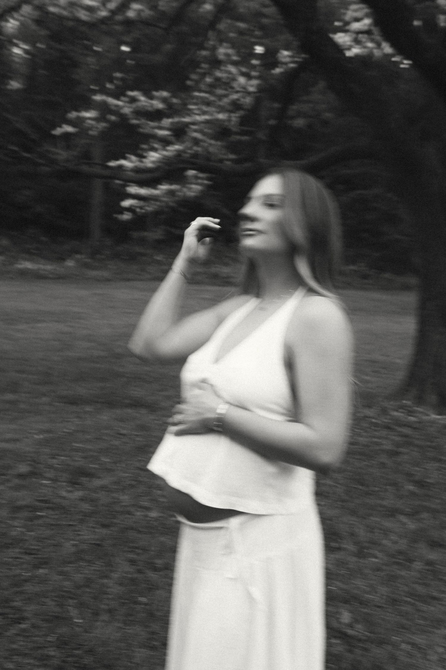 Dreamy black and white portrait of pregnant woman in white dress among trees.