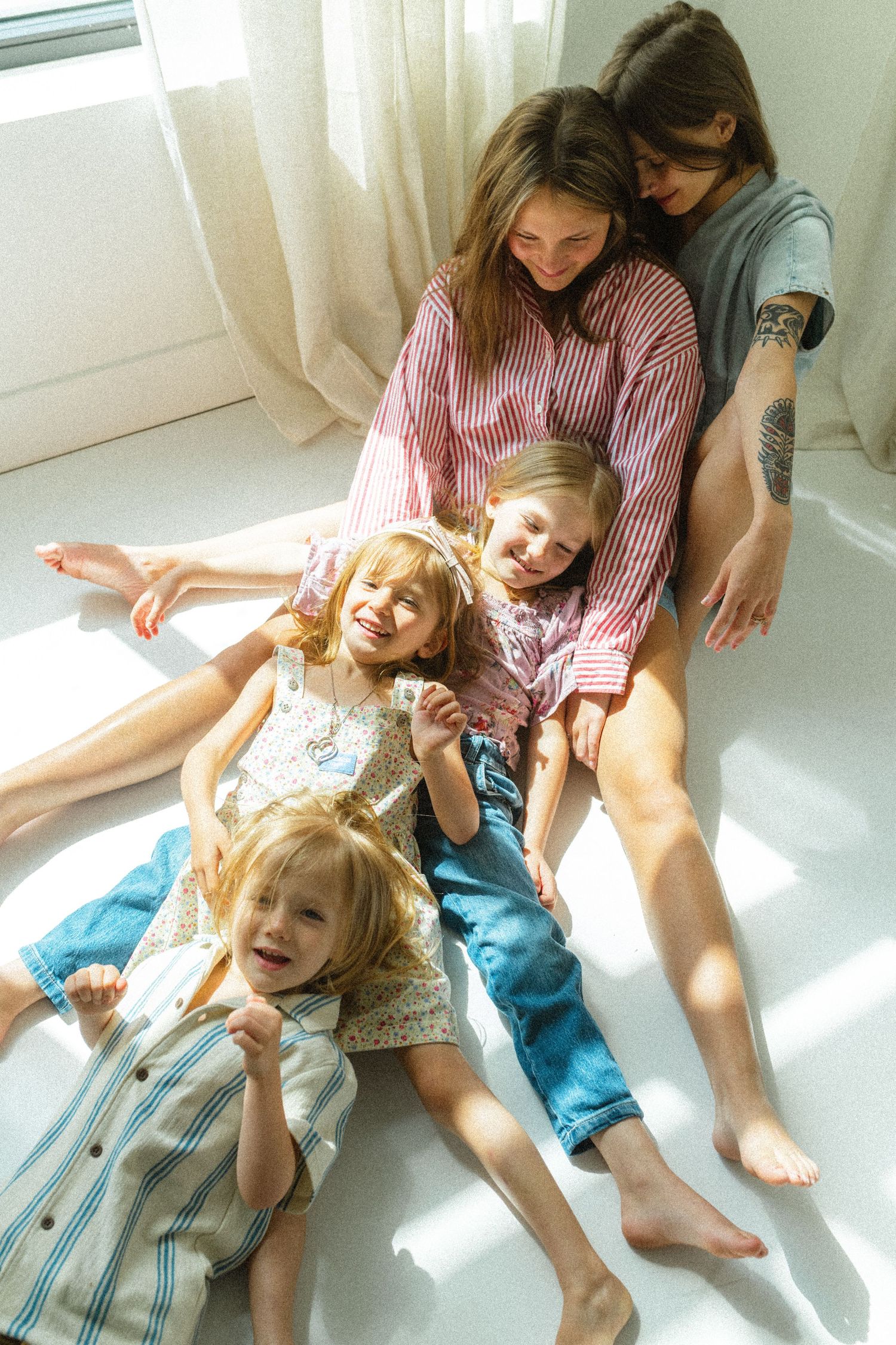 Two mothers sitting by a sunny window with three young children laughing and relaxing together.