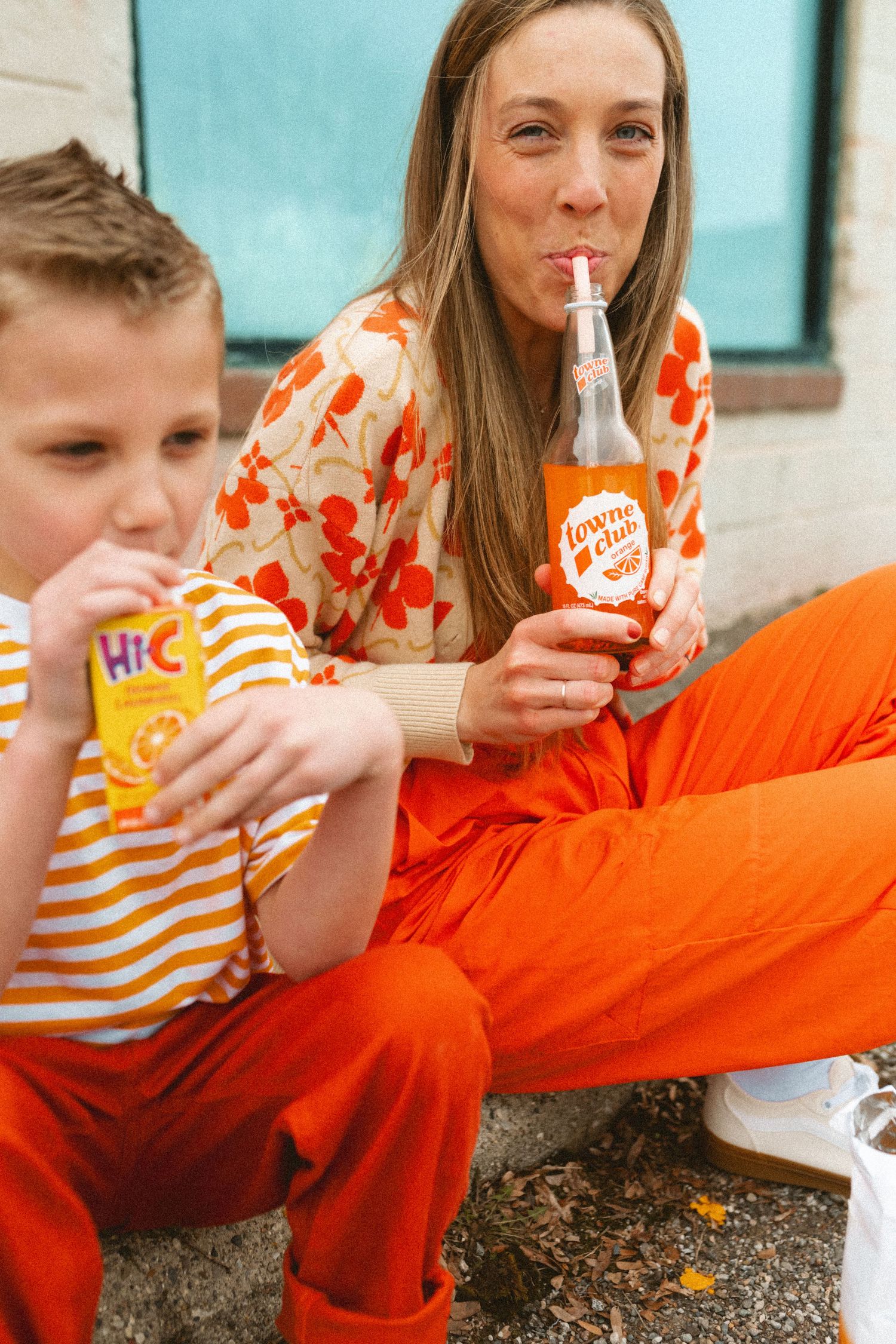Woman sipping Town Club orange soda while boy drinks Hi-C juice box outdoors.