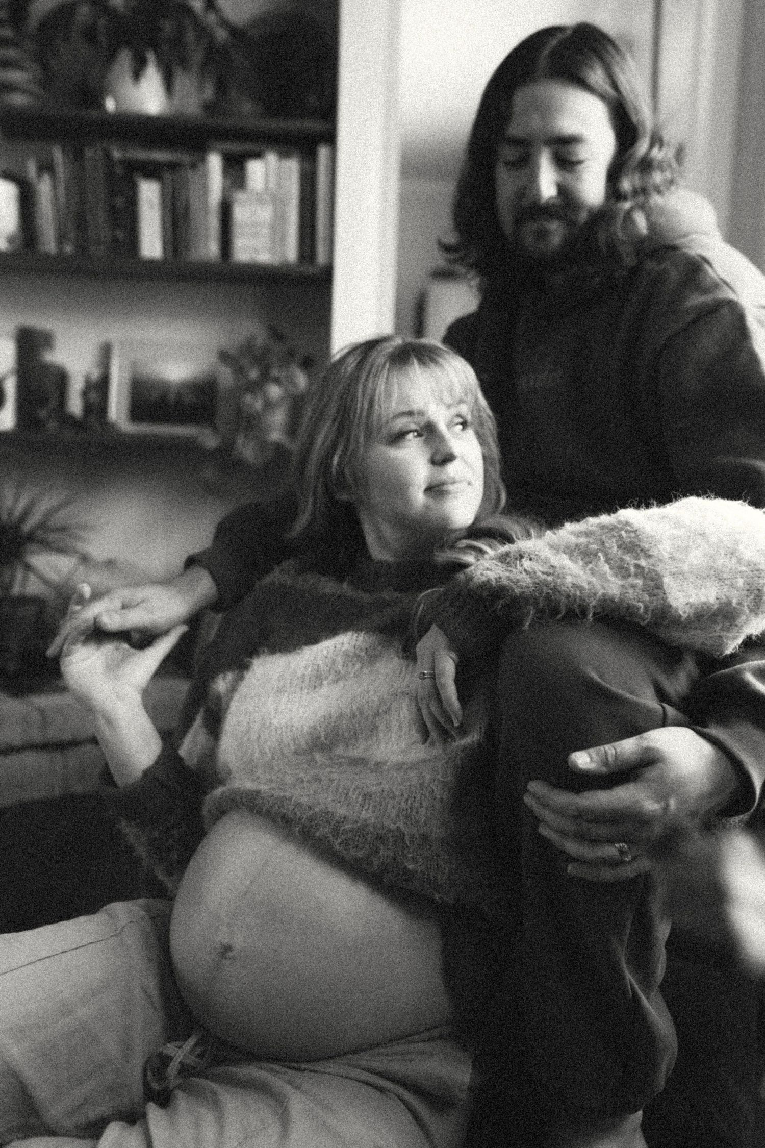 Black and white photo of a pregnant woman reclining with her partner in a cozy home library.
