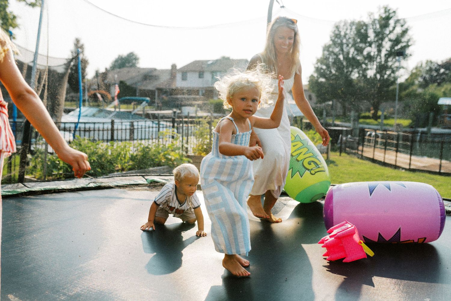 Children playing on a backyard trampoline on a sunny summer day with colorful inflatable toys.