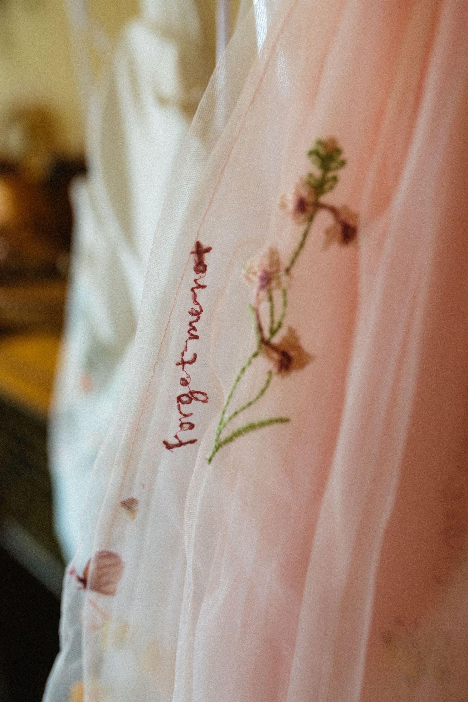 Close-up of embroidered forget-me-not flowers on sheer pink veil.