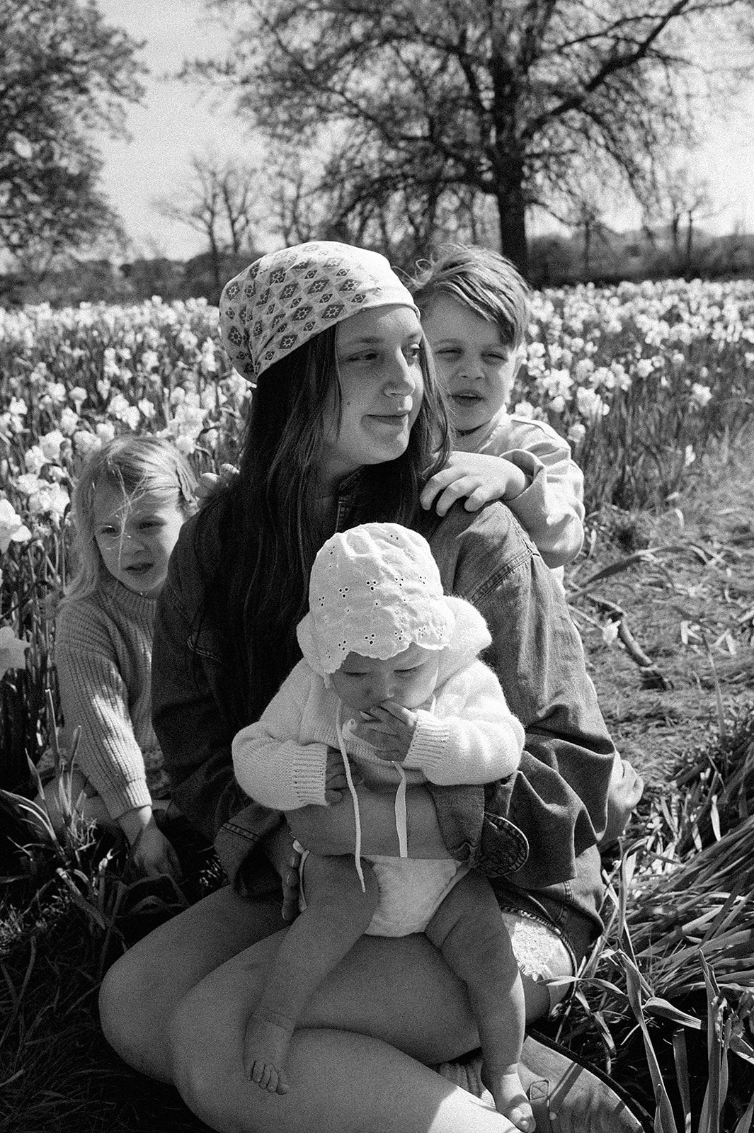 Black and white photo of a young mother sitting in a flower field with three children around her.