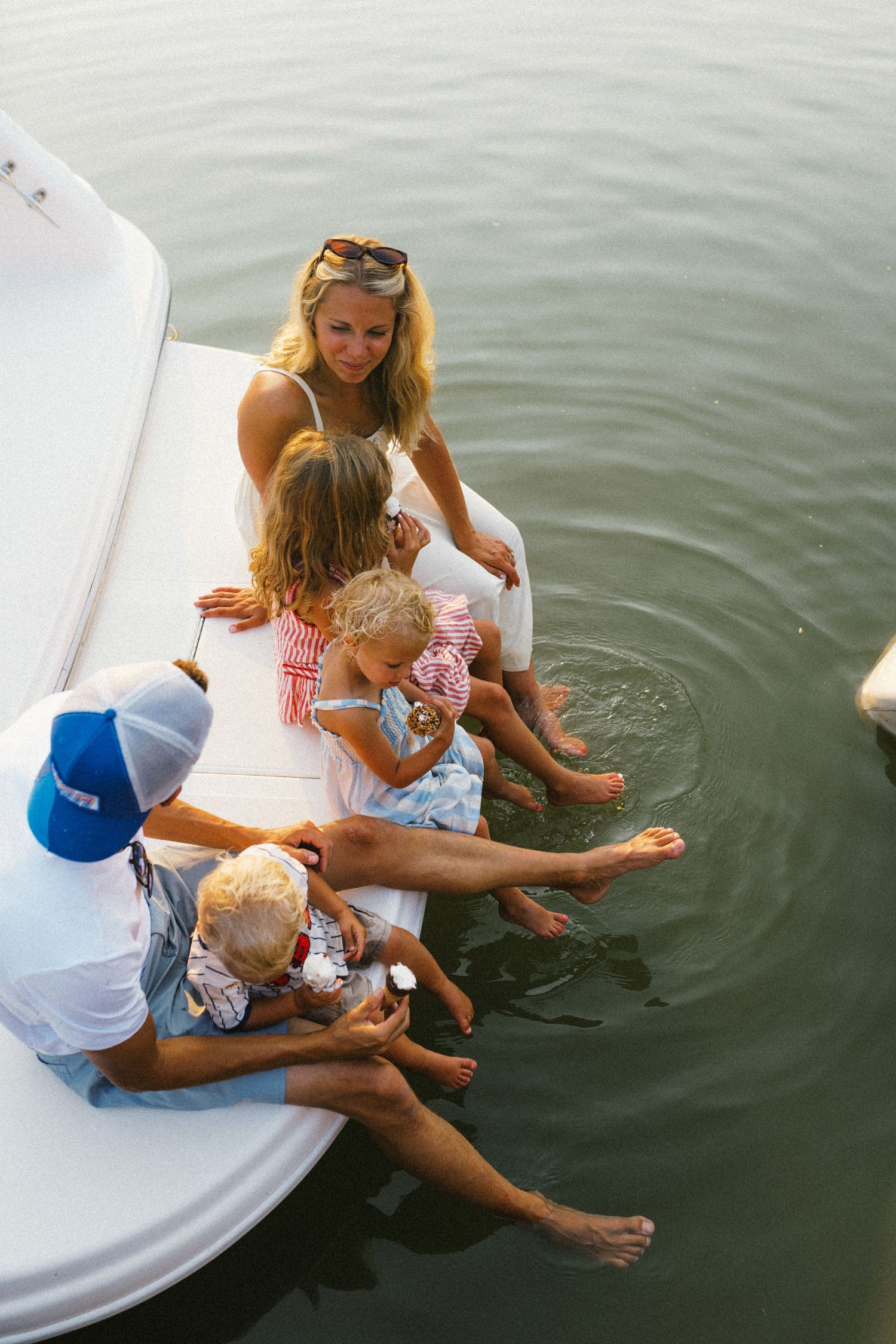 Family with young children sitting on edge of boat dipping feet in calm lake water.
