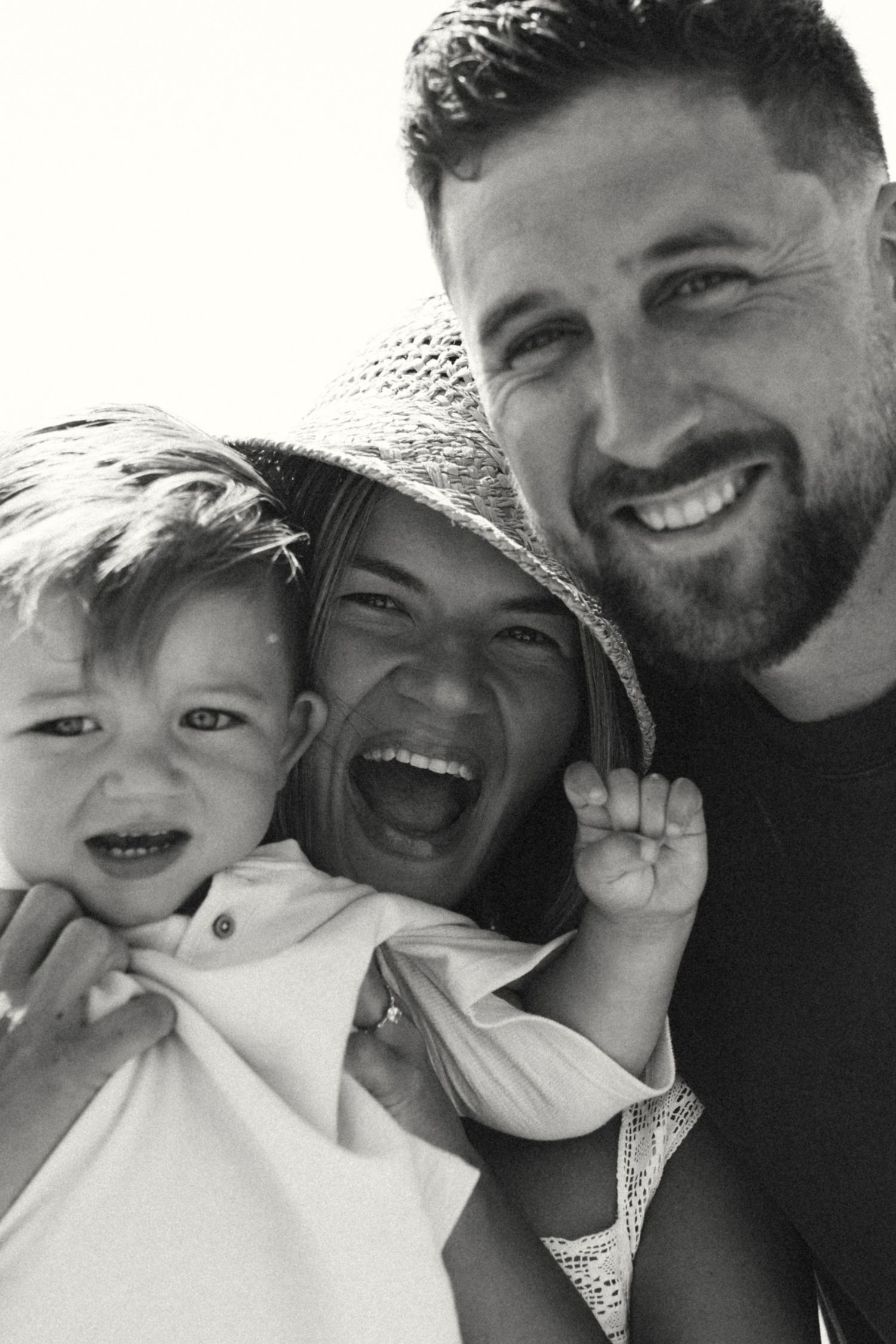 Black and white close-up portrait of smiling family with young toddler and bearded father.