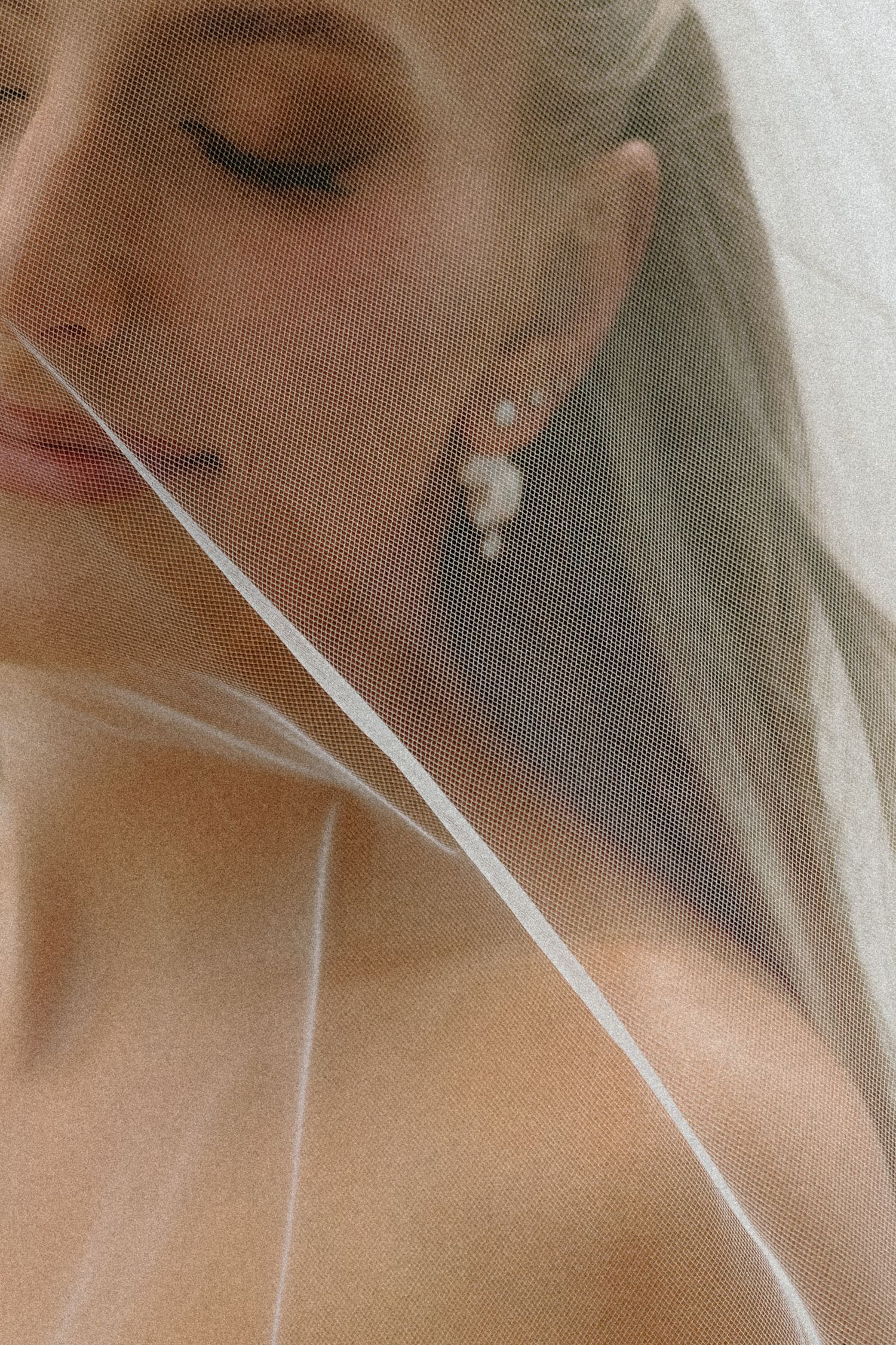 Close-up portrait of bride wearing pearl earrings with soft veil draped across her face.