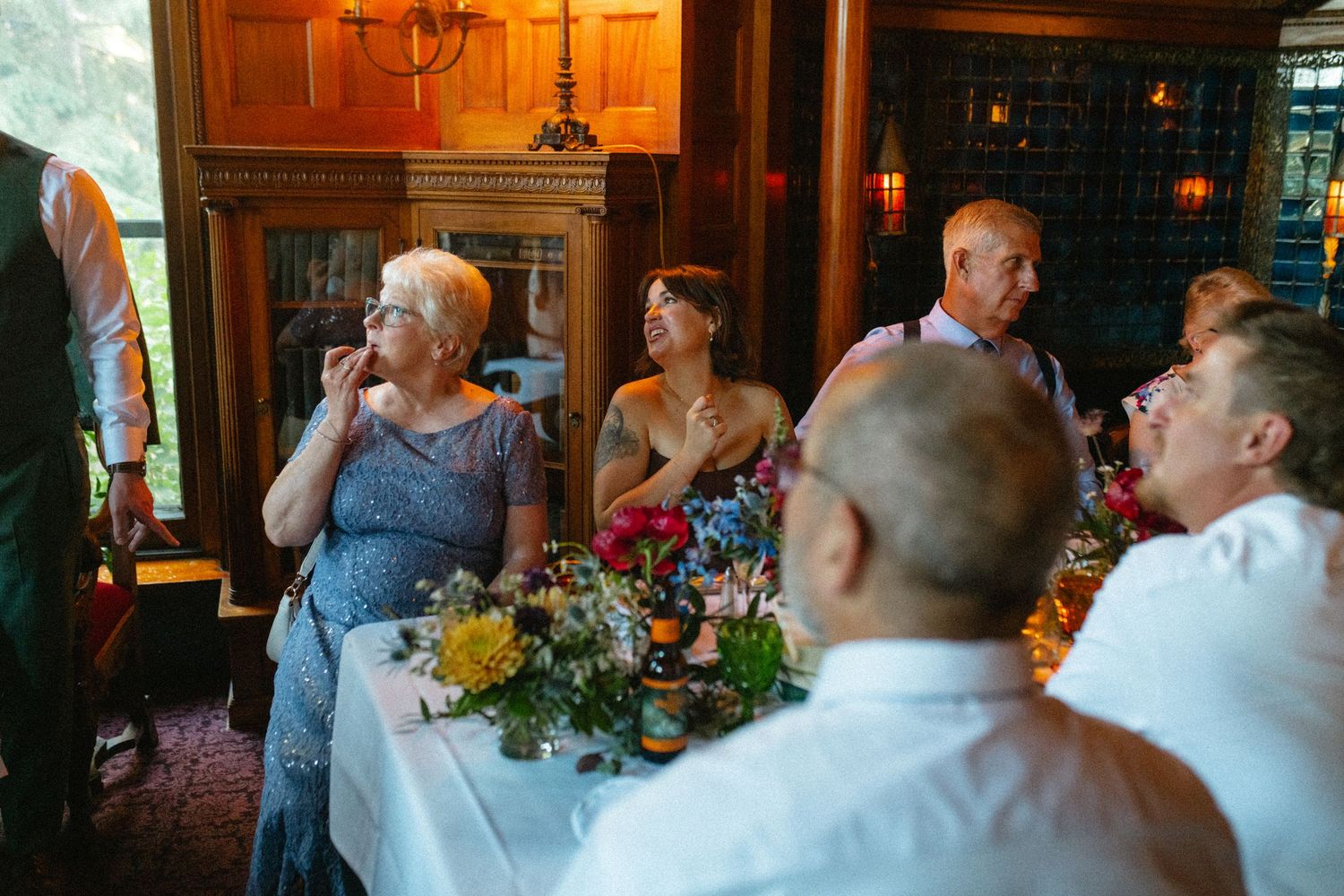 Wedding guests laughing and enjoying speeches at elegantly decorated reception dinner table.