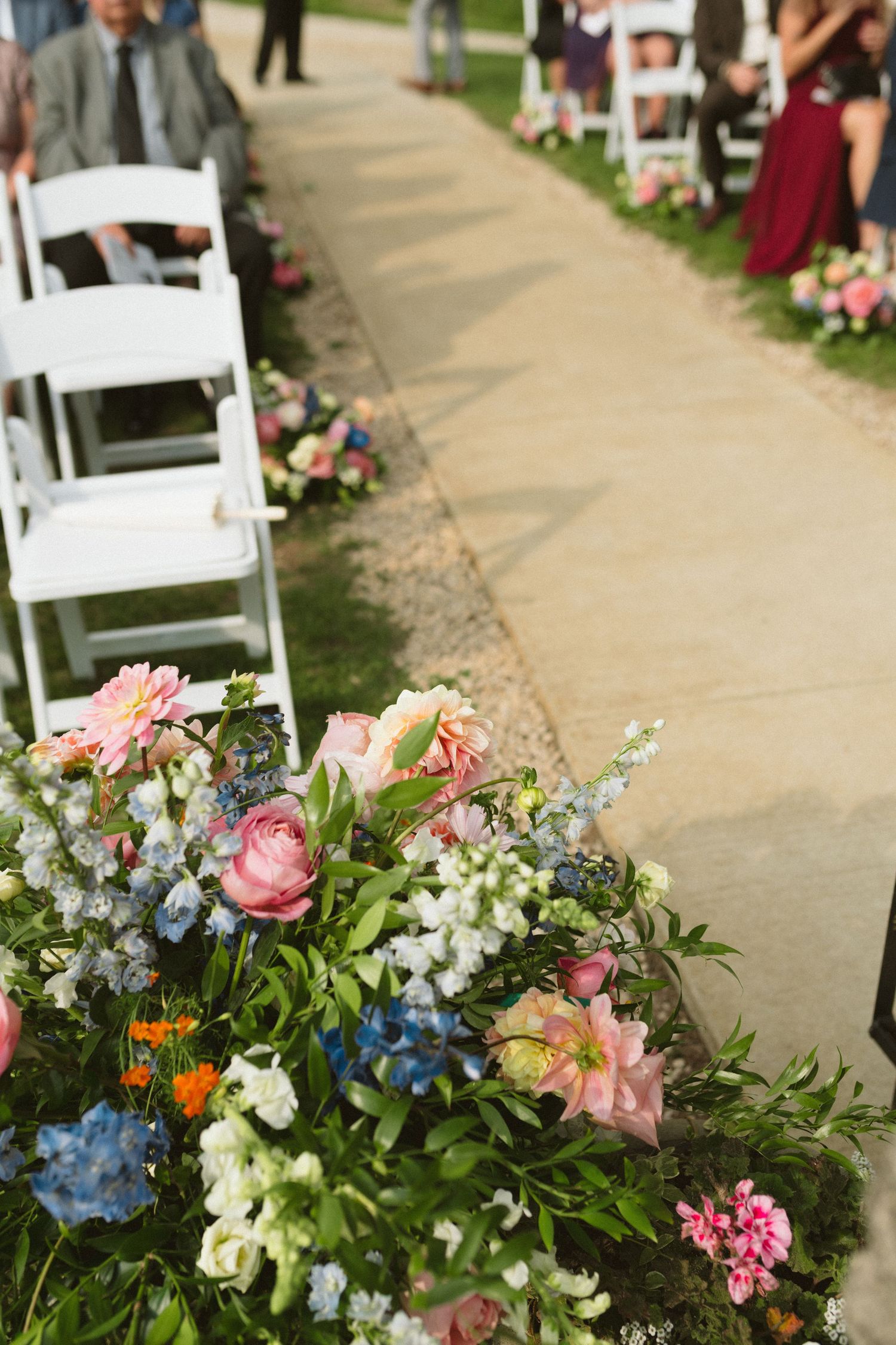Colorful floral arrangements of pink, blue, and white blooms lining outdoor wedding aisle.