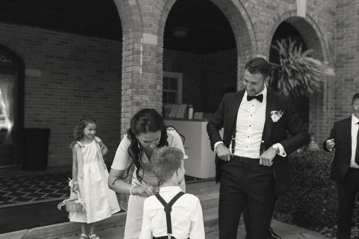 Black and white photo of bride and groom with flower girl and ring bearer outside brick church.