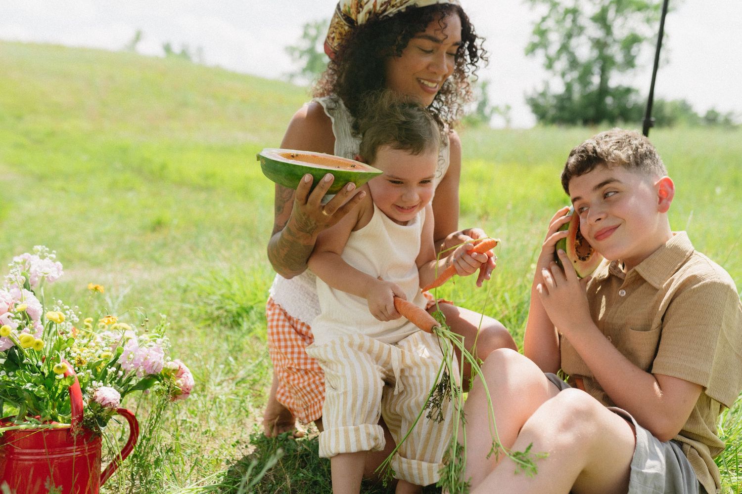 Family enjoying watermelon picnic together in sunny green meadow with wildflowers.