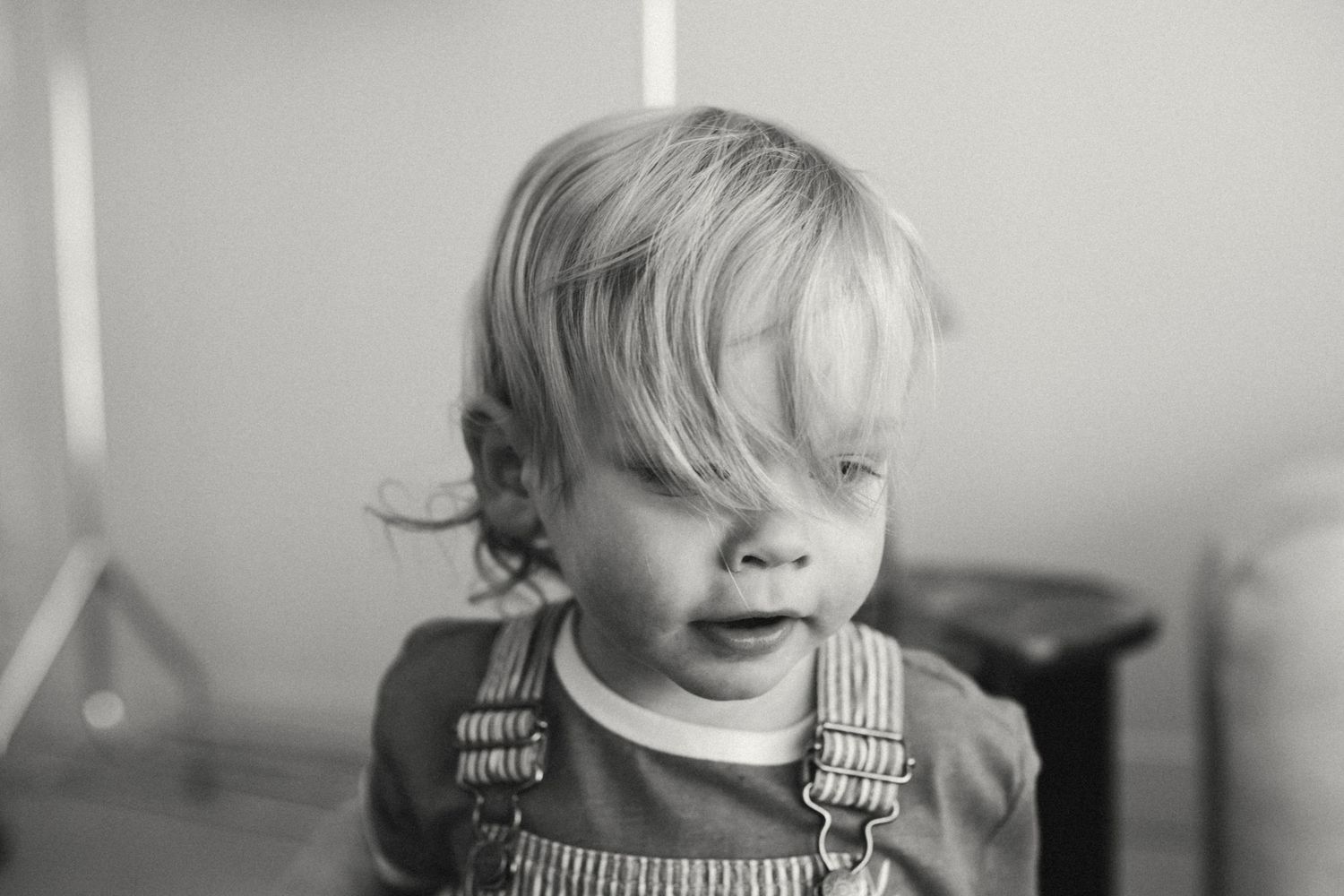 Black and white portrait of a blonde toddler in striped overalls looking away.