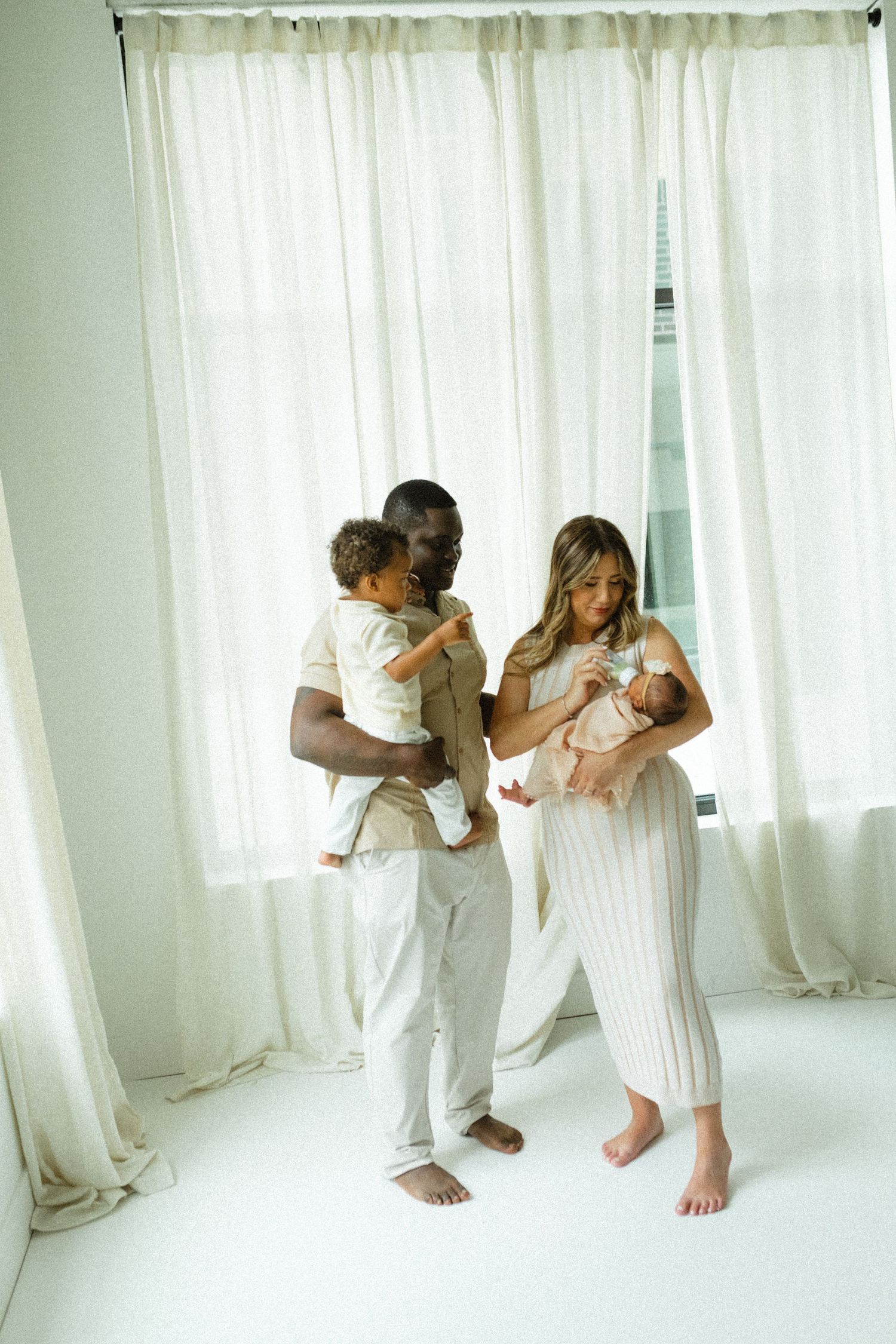 Interracial family with newborn and toddler posing in bright white studio for family portrait.