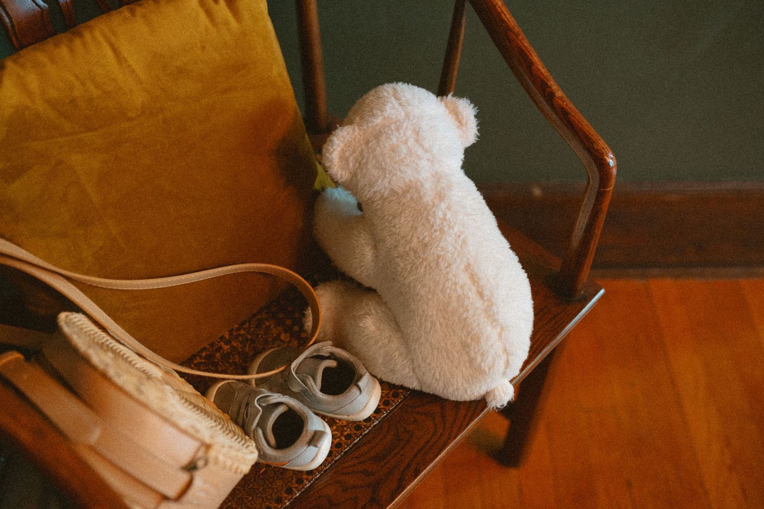 White stuffed teddy bear and tiny baby shoes on a vintage wooden chair at a wedding venue.