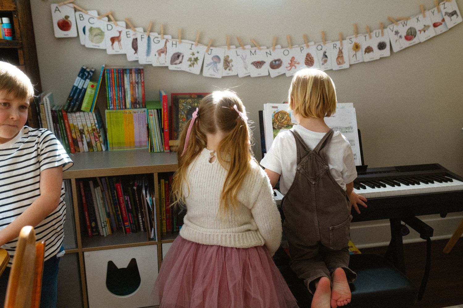 Three children gathered around a piano in a colorful home music room.
