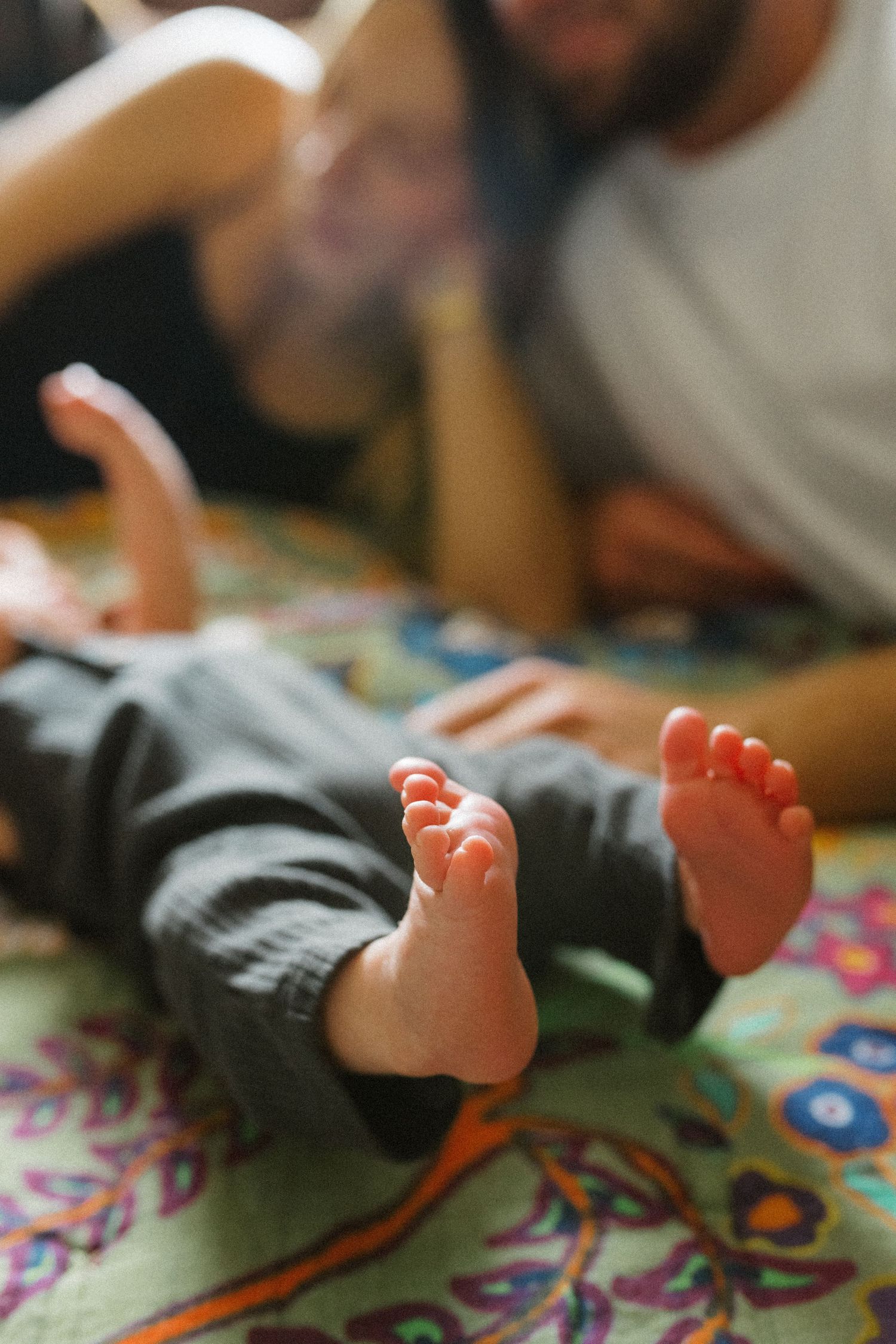 Newborn baby feet in foreground with blurred parents smiling on colorful floral blanket.