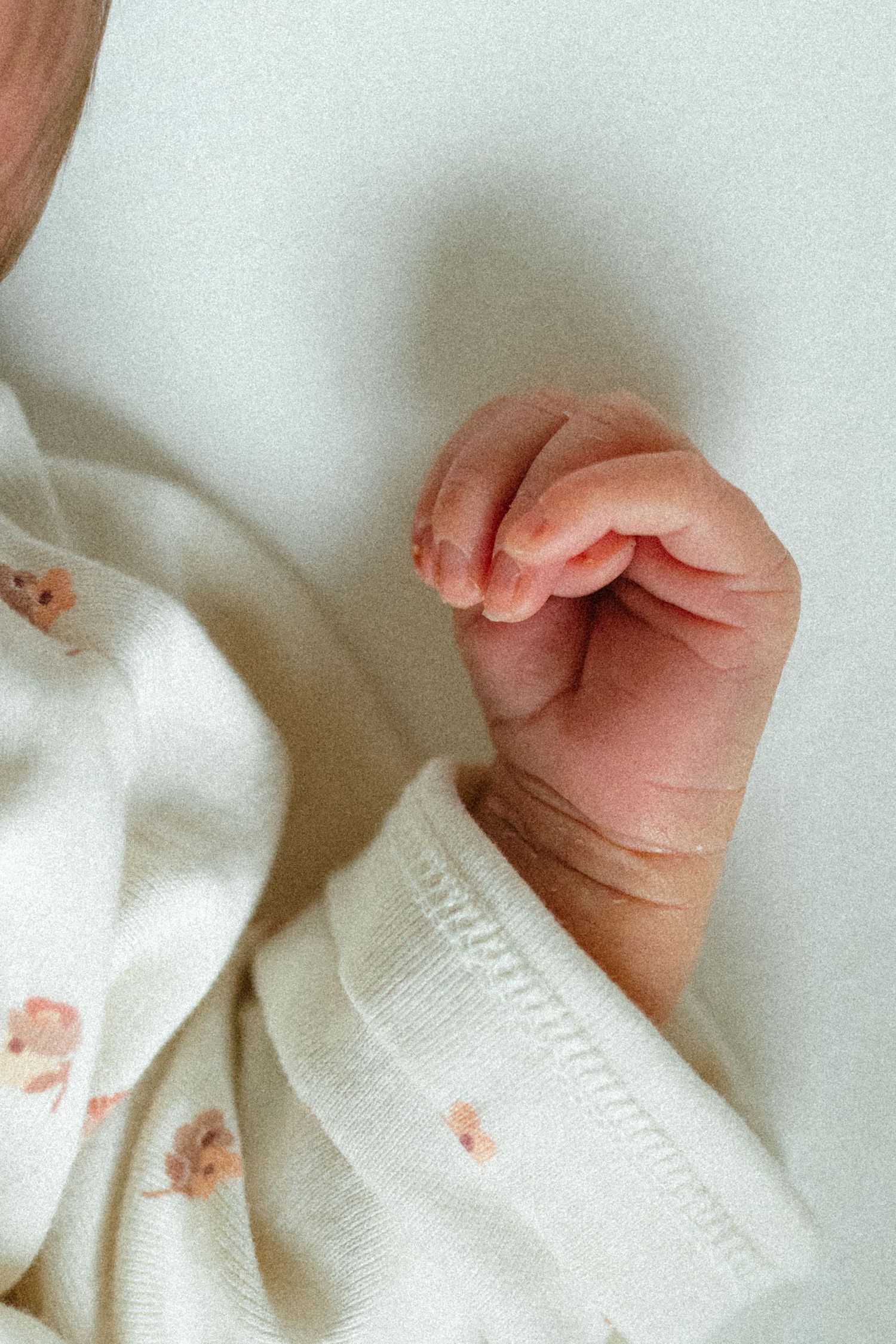 Close-up of a newborn baby's tiny hand in a floral onesie against a white background.