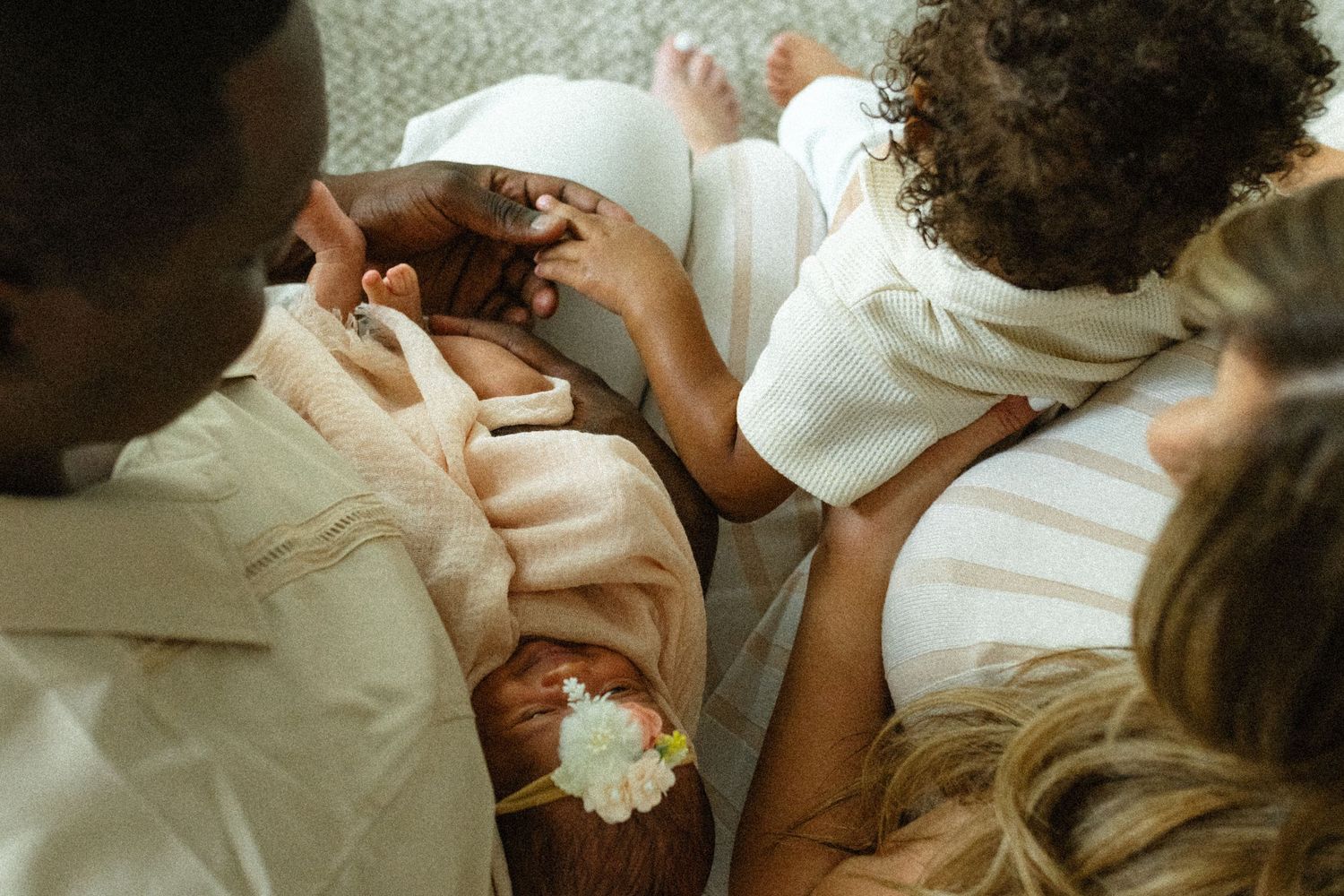Overhead view of parents and toddler lovingly gathered around newborn baby with flower headband.