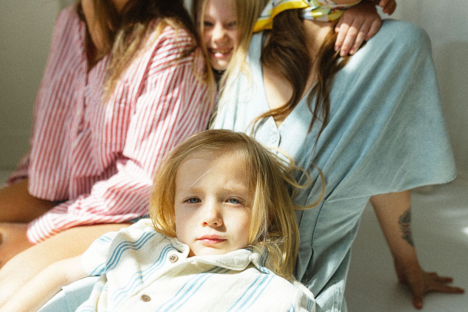 Young girl in light blue pajamas sitting in front of women and children in cozy indoor setting.