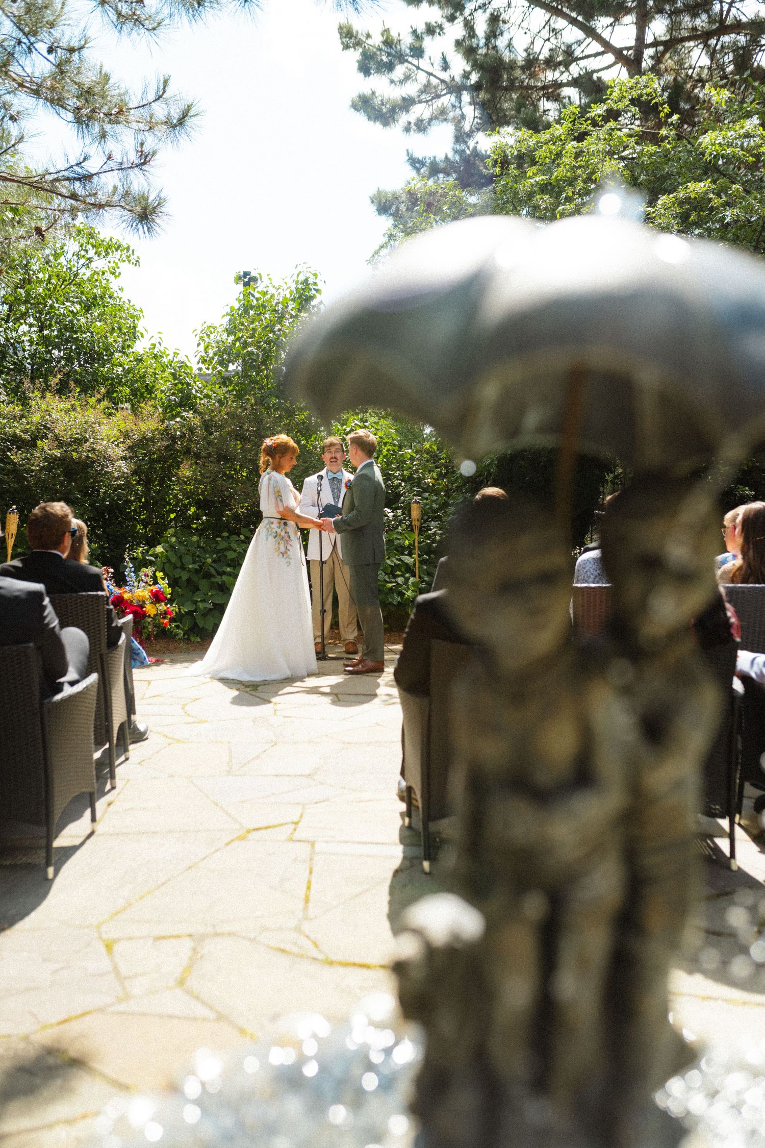 Outdoor wedding ceremony on stone patio with bride and groom exchanging vows surrounded by lush greenery.