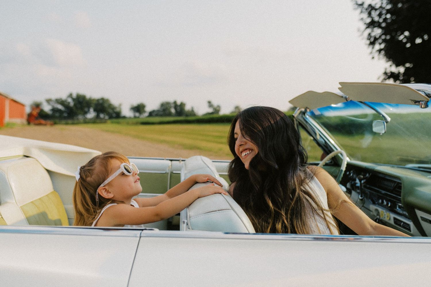 Mother and daughter laughing together in a white vintage convertible car outdoors.